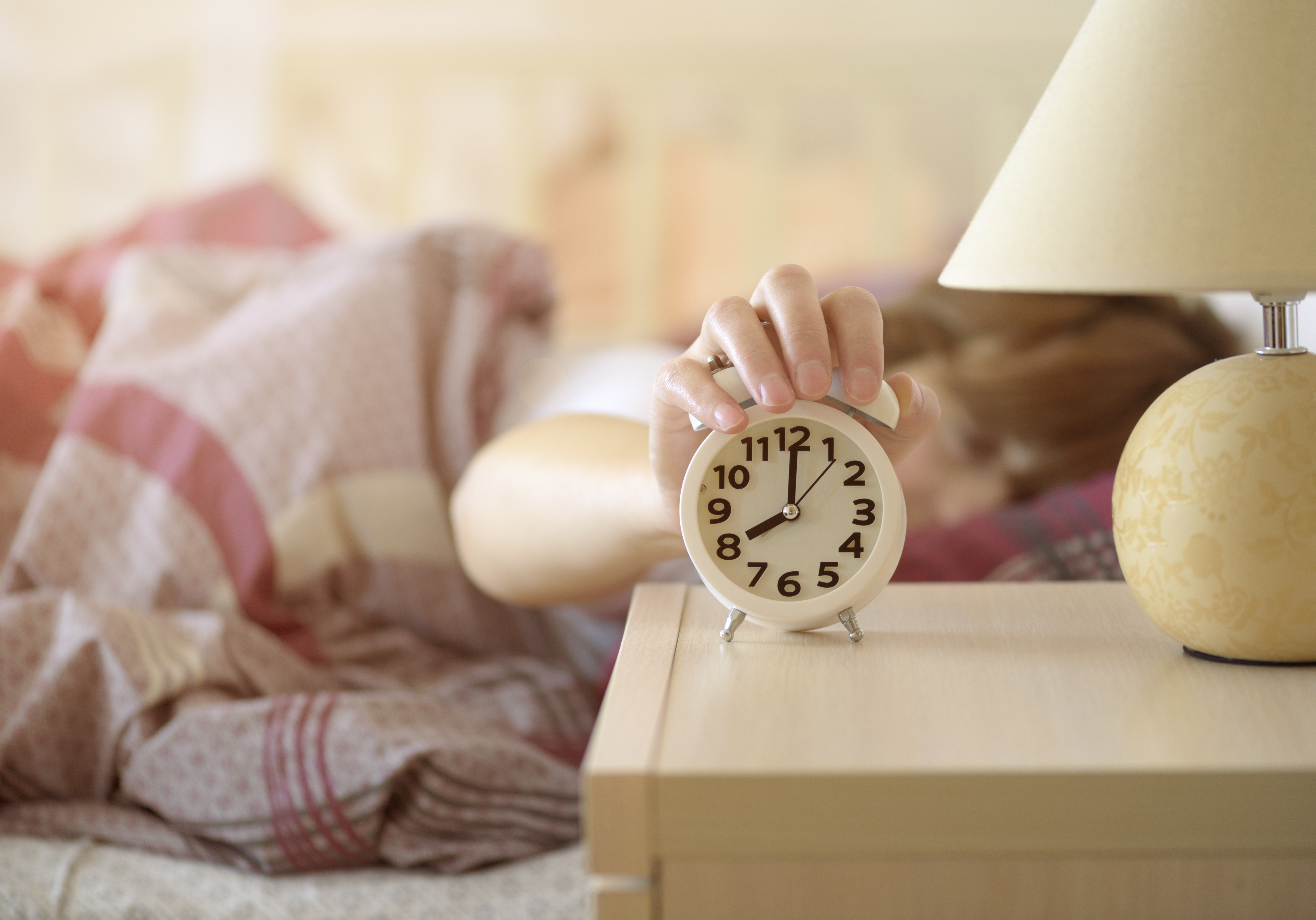 Woman turns off the alarm clock waking up in the morning from a call. | Source: Shutterstock