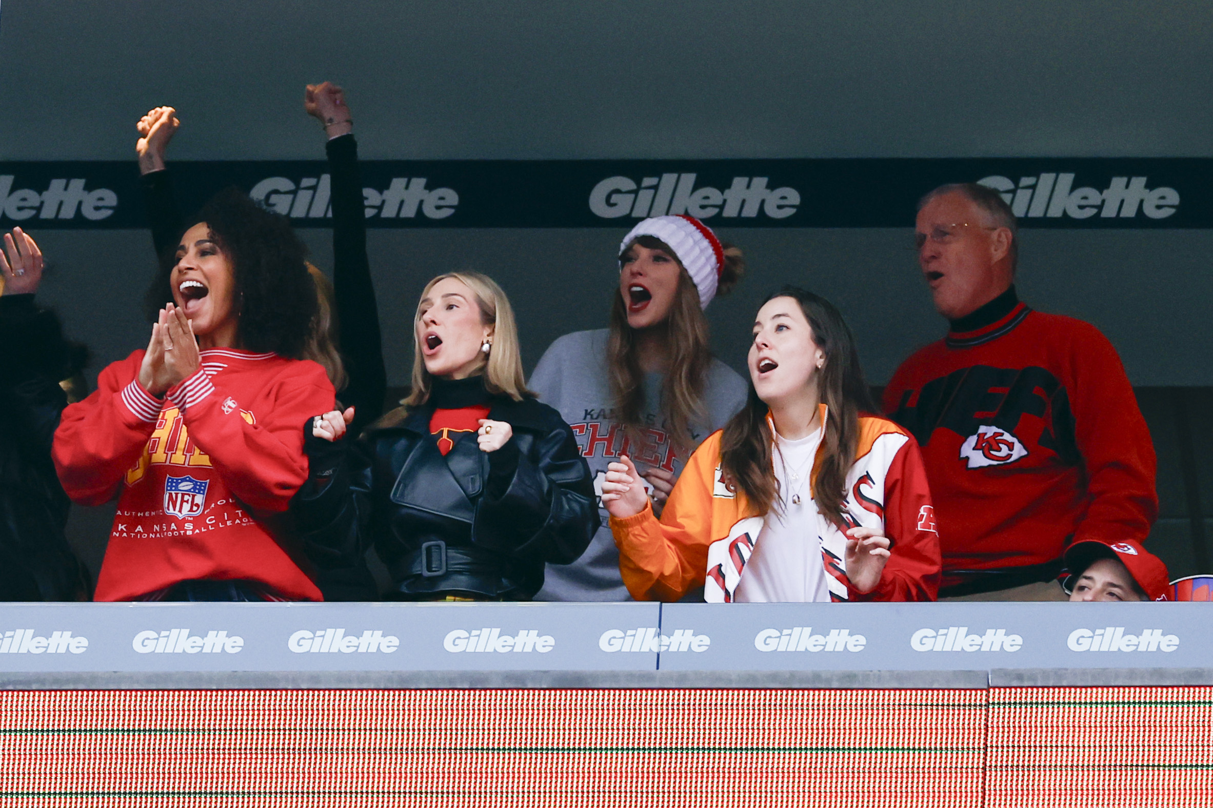 Taylor Swift, wearing a gray Kansas City Chiefs sweatshirt and a red-and-white knit hat, cheers from a suite after Chiefs tight end Travis Kelce makes a first-quarter catch during a game against the New England Patriots at Gillette Stadium on December 17, 2023. The Chiefs won 27-17.