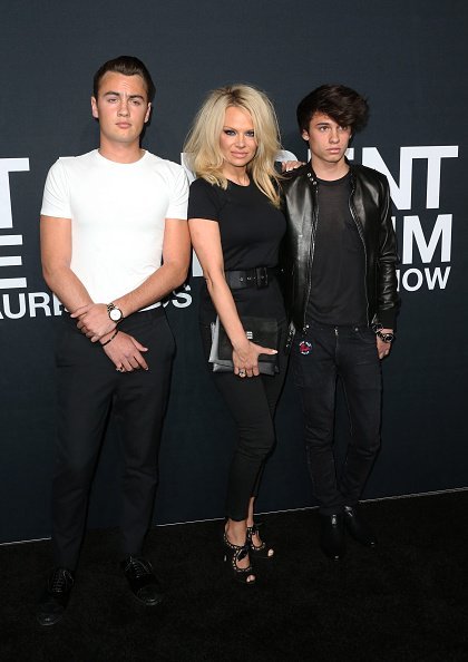 Pamela Anderson (center) and her sons Brandon Lee (L) and Dylan Lee attend the Saint Laurent show at The Hollywood Palladium on February 10, 2016, in Los Angeles, California. | Source: Getty Images.