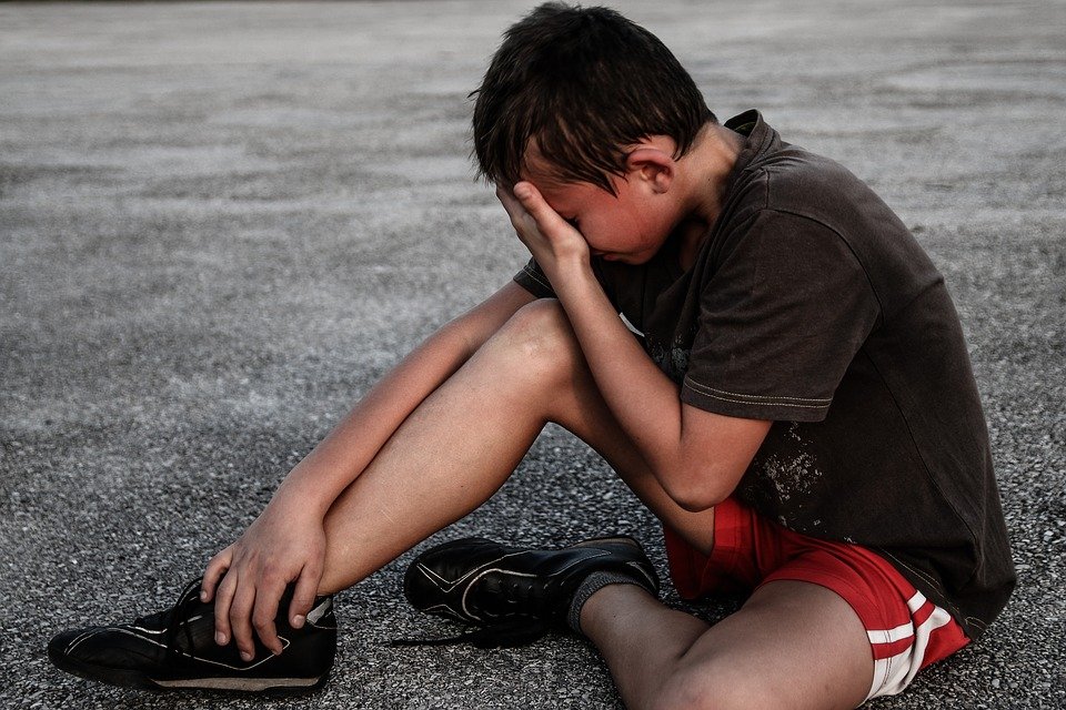 Niño afligido sentado en el suelo llorando con la mano sobre su rostro. | Foto: Pixabay