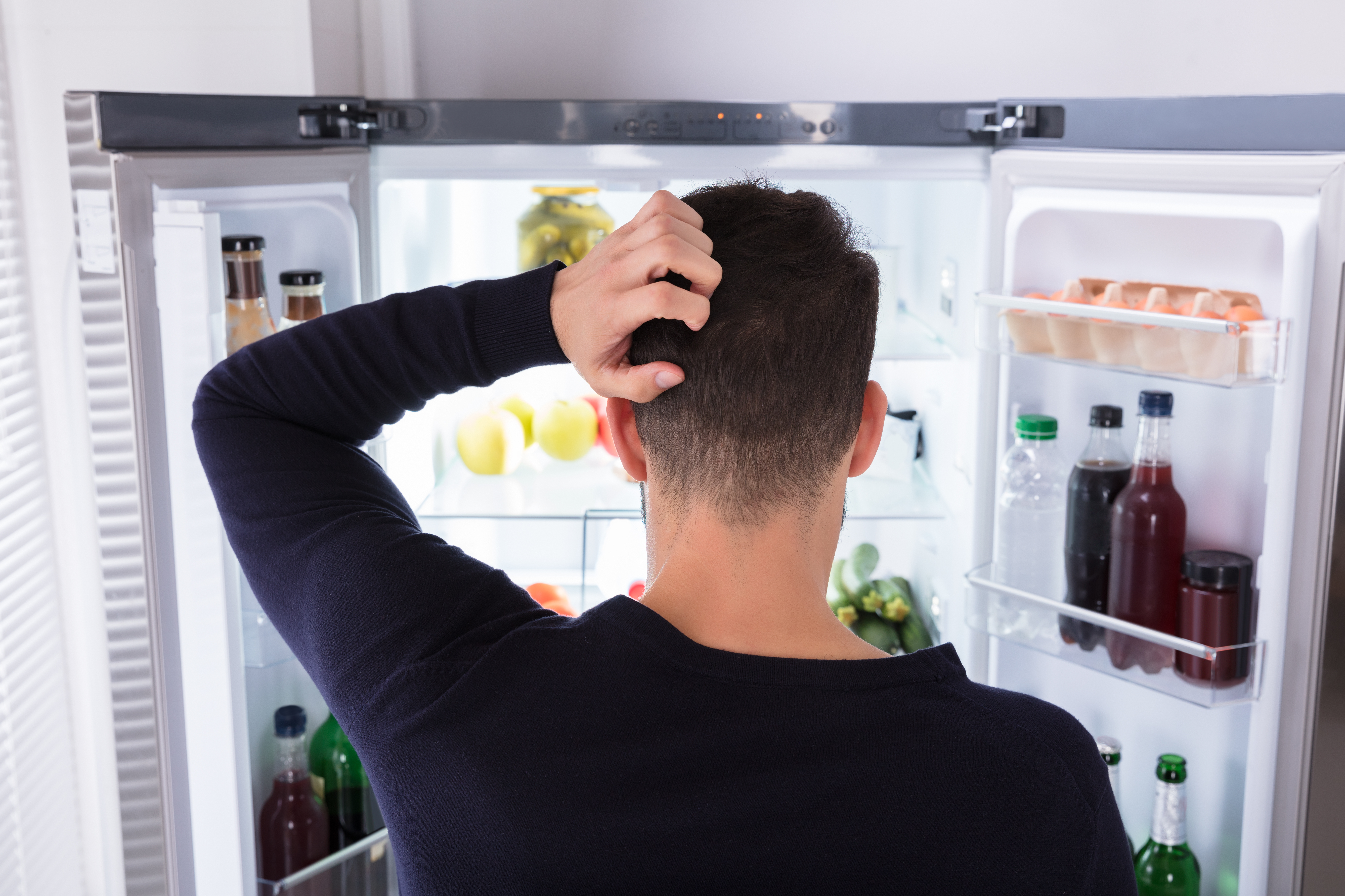 Rear View Of A Confused Young Man Looking At Food In Refrigerator. | Source: Shutterstock