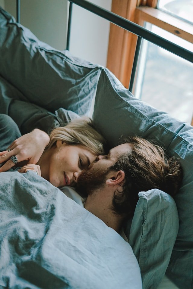 Men kissing woman on forehead while laying in bed | Source: Unsplash