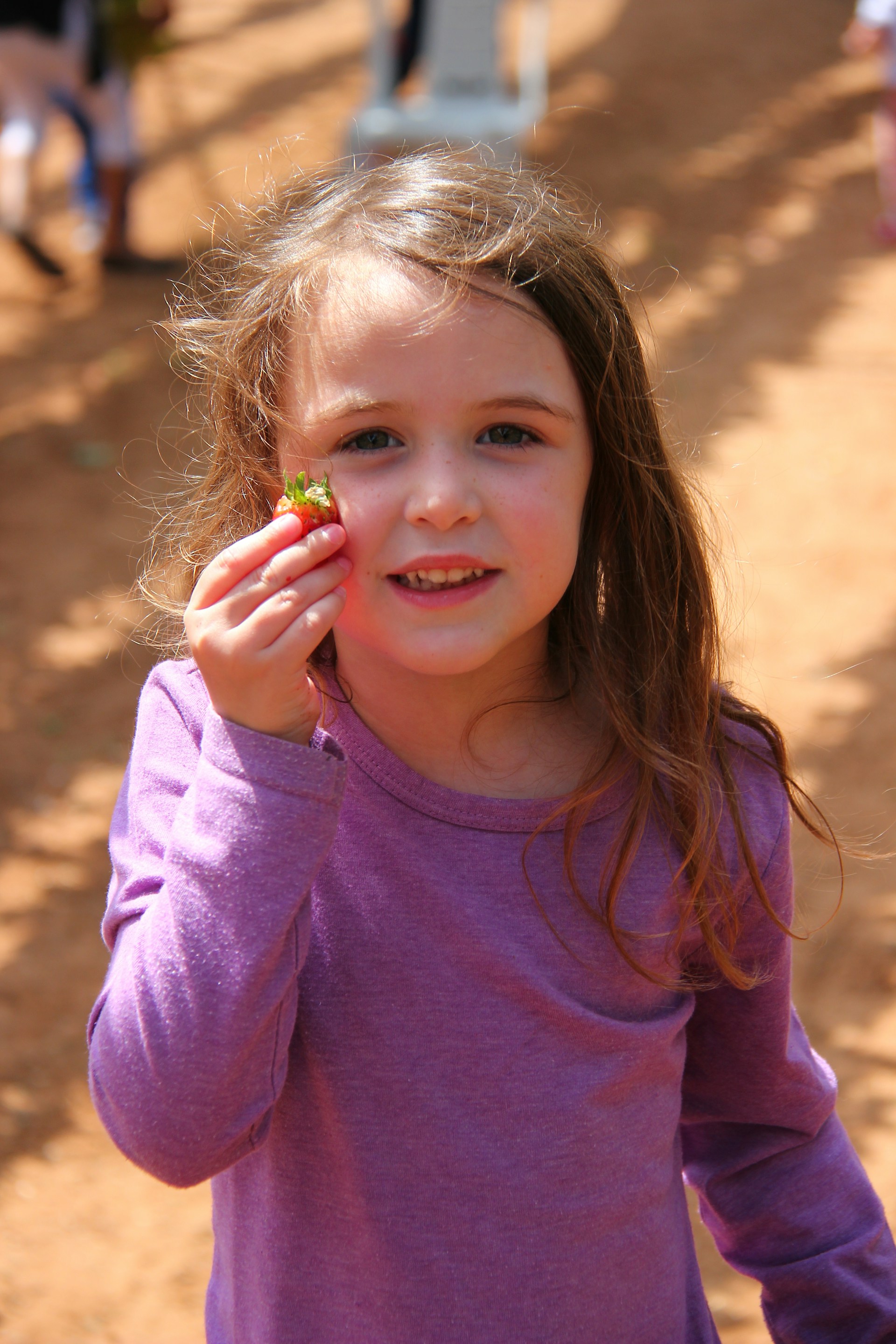 A little girl holding a strawberry and smiling | Source: Unsplash