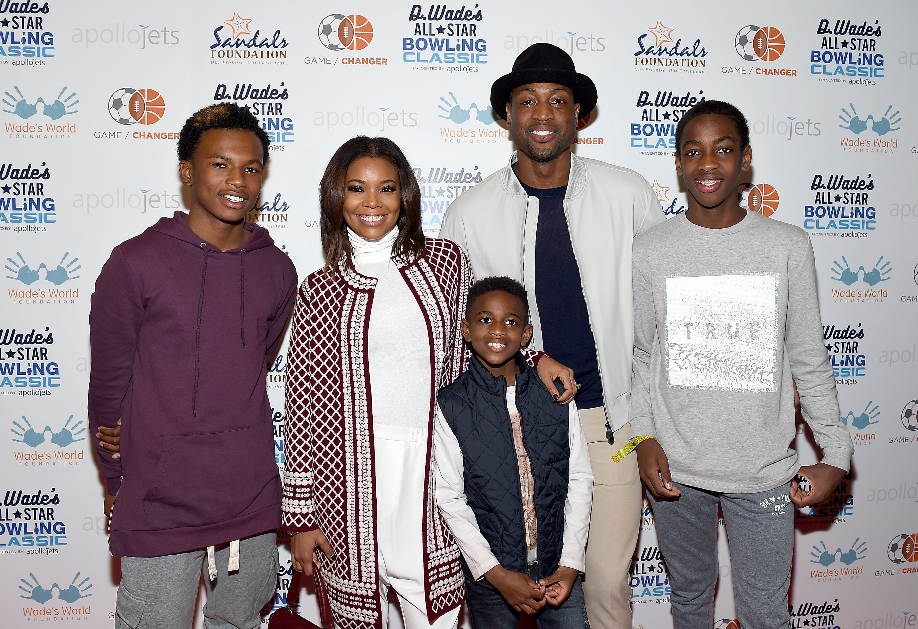 Zaire Wade, Gabrielle Union, Xavier Zechariah Wade, Dwyane Wade, and Zaya Wade pose together for a family portrait in front of a branded backdrop at a charity bowling fundraiser.