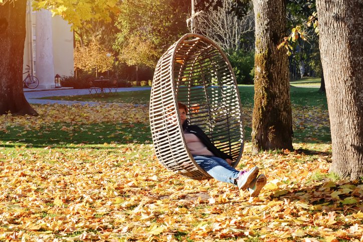 Mädchen schwingt im Park auf hängendem eiförmigem Stuhl im Freien inmitten der gefallenen Blätter. I Quelle: Getty Images