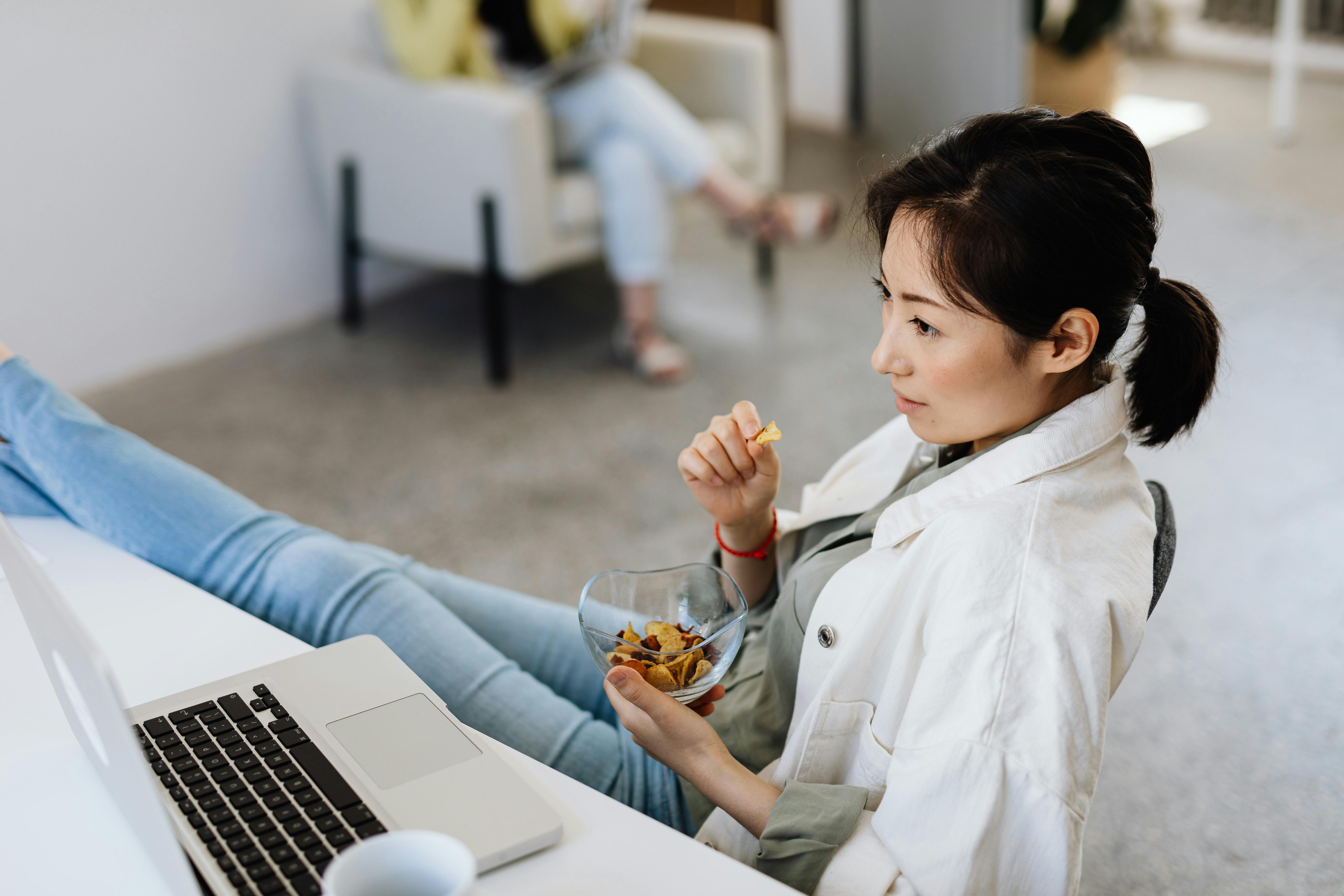 A woman eating a snack while working at her computer. | Source: Pexels