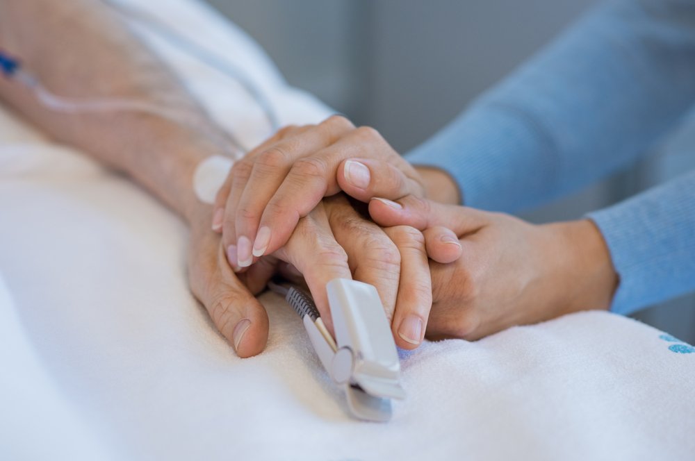 Persona sosteniendo la mano de un enfermo recostado en la cama de un hospital. | Foto: Shutterstock