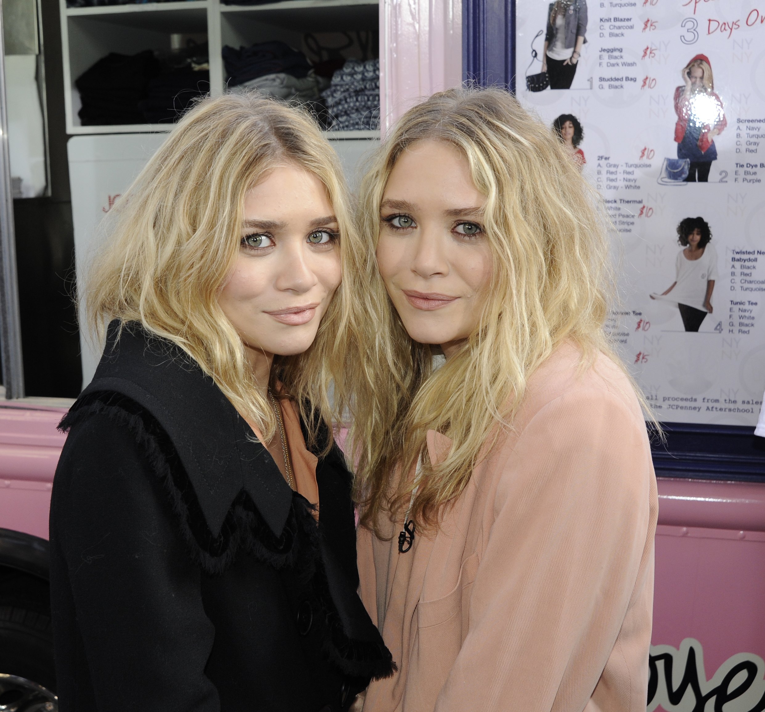 Mary-Kate and Ashley Olsen pose closely during a TV appearance, leaning in with soft smiles. Their loose waves and neutral outfits give the moment a relaxed, polished feel.