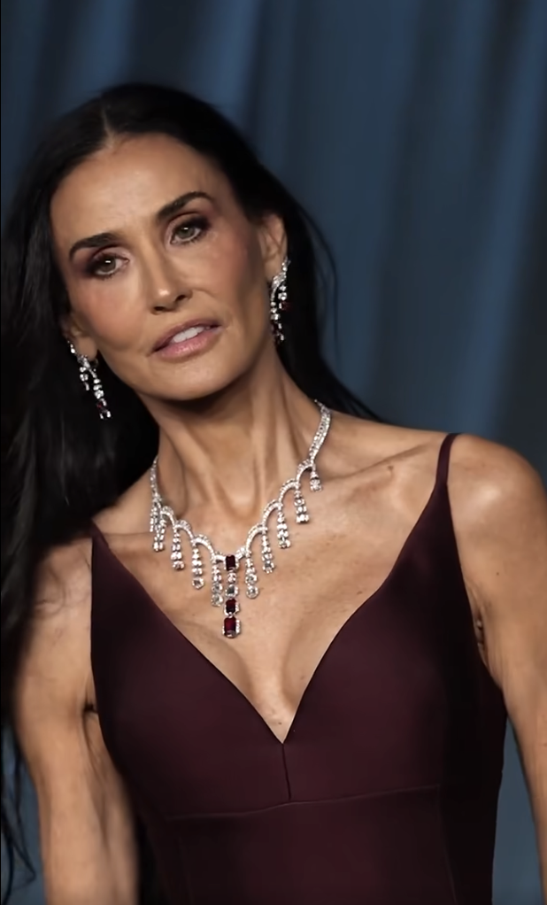Demi Moore tilts her head ever so slightly, her eyes focused with quiet intensity. With one hand brushing through her hair, she radiates calm control, letting the sharp neckline and ruby-studded diamonds do the talking. | Source: Facebook/TooFab