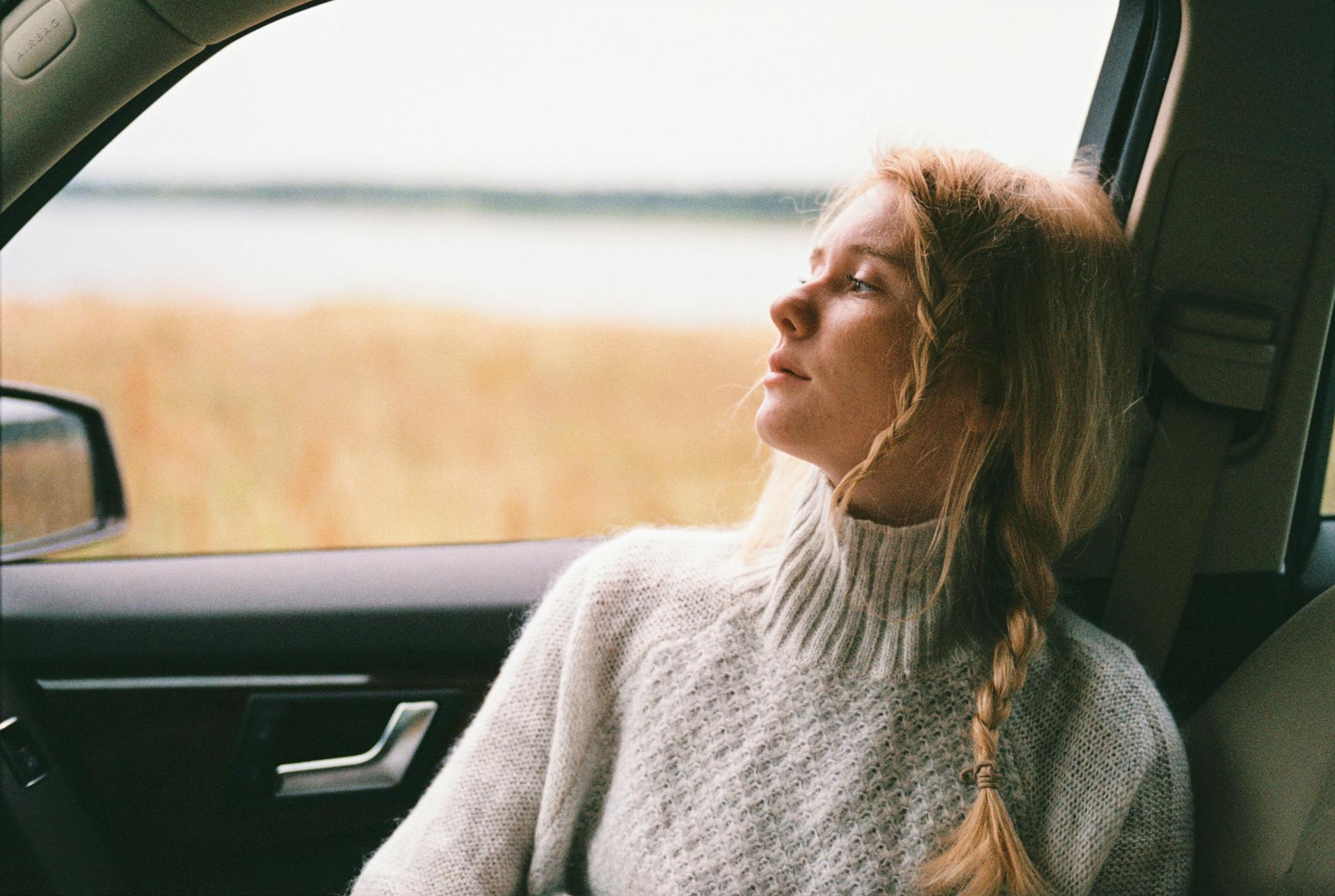 A woman in a sweater sitting inside a car and thinking | Source: Pexels
