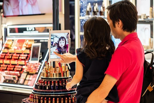  Father and daughter play with a digital tablet at an Estée Lauder store.| Photo: Getty Images.