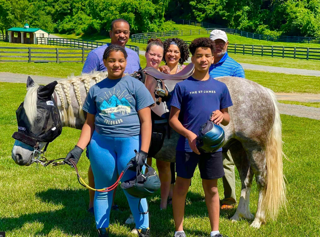 Cameron and Carys Fairfax stand beside their parents, Justin and Cerina Fairfax, during a horseback riding outing | Source: Facebook/justin.fairfax.2025