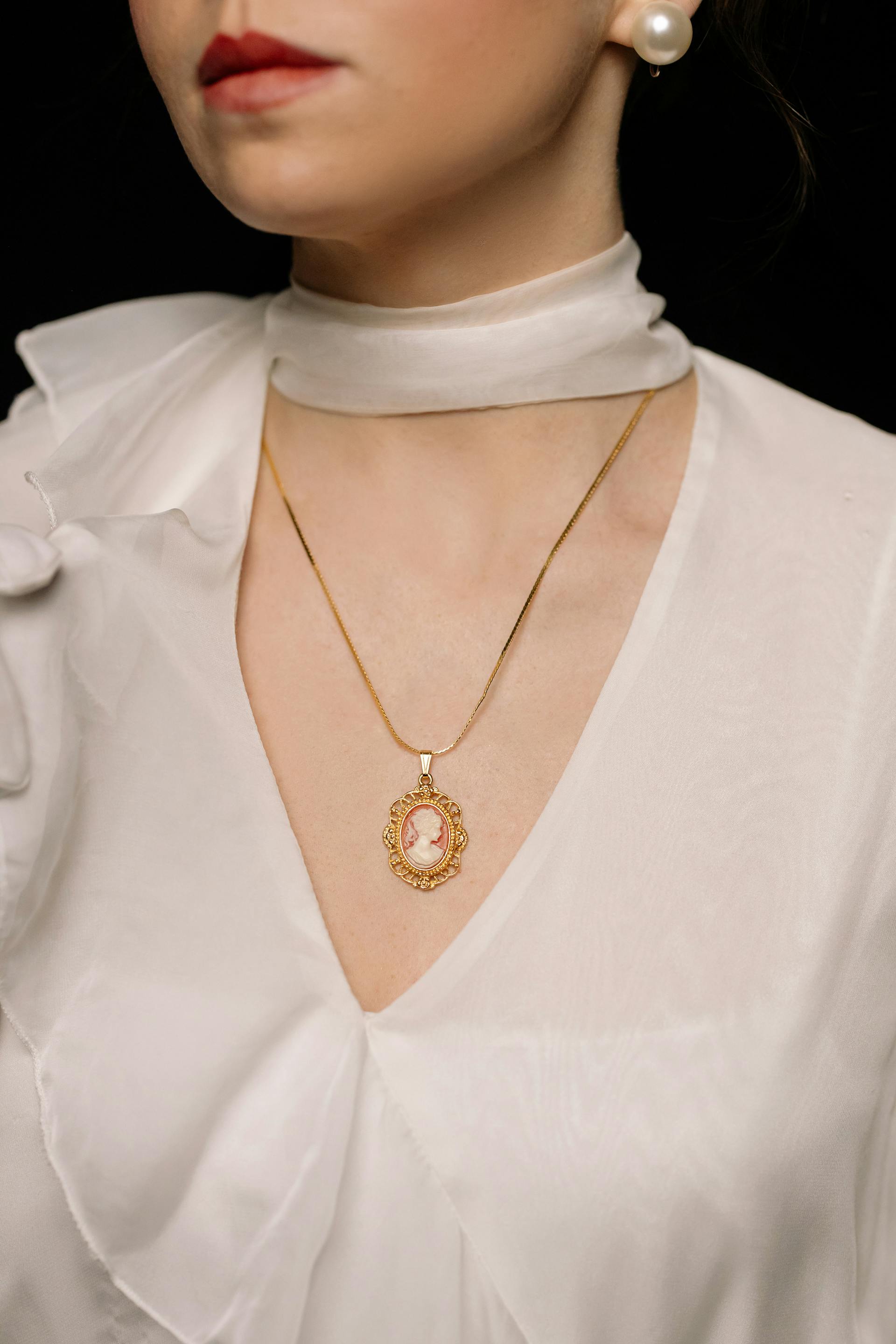 A close-up of a woman wearing pearl earrings and a gold necklace with a pendant | Source: Pexels