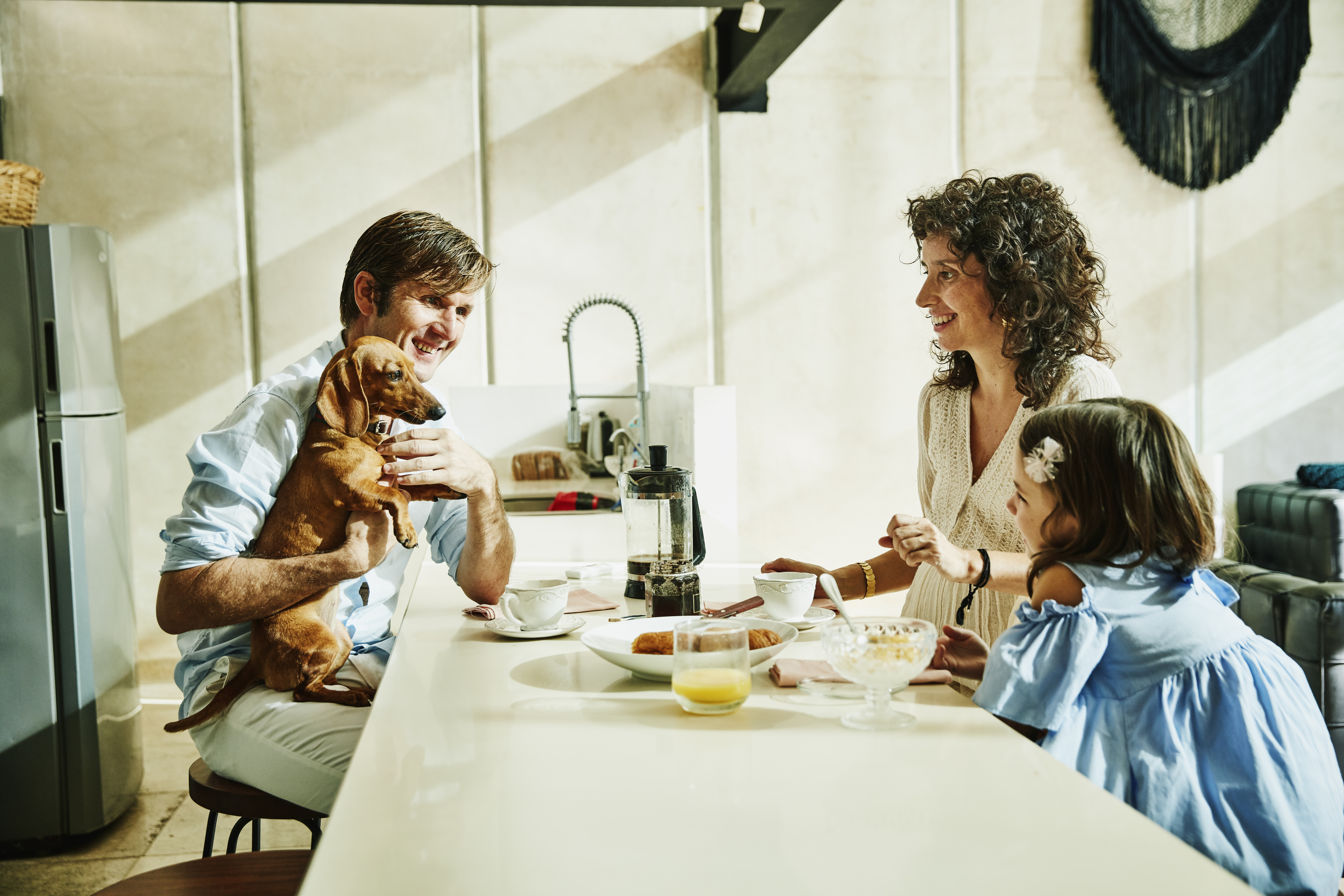Smiling father holding dog while having breakfast with family in kitchen | Source: Getty Images