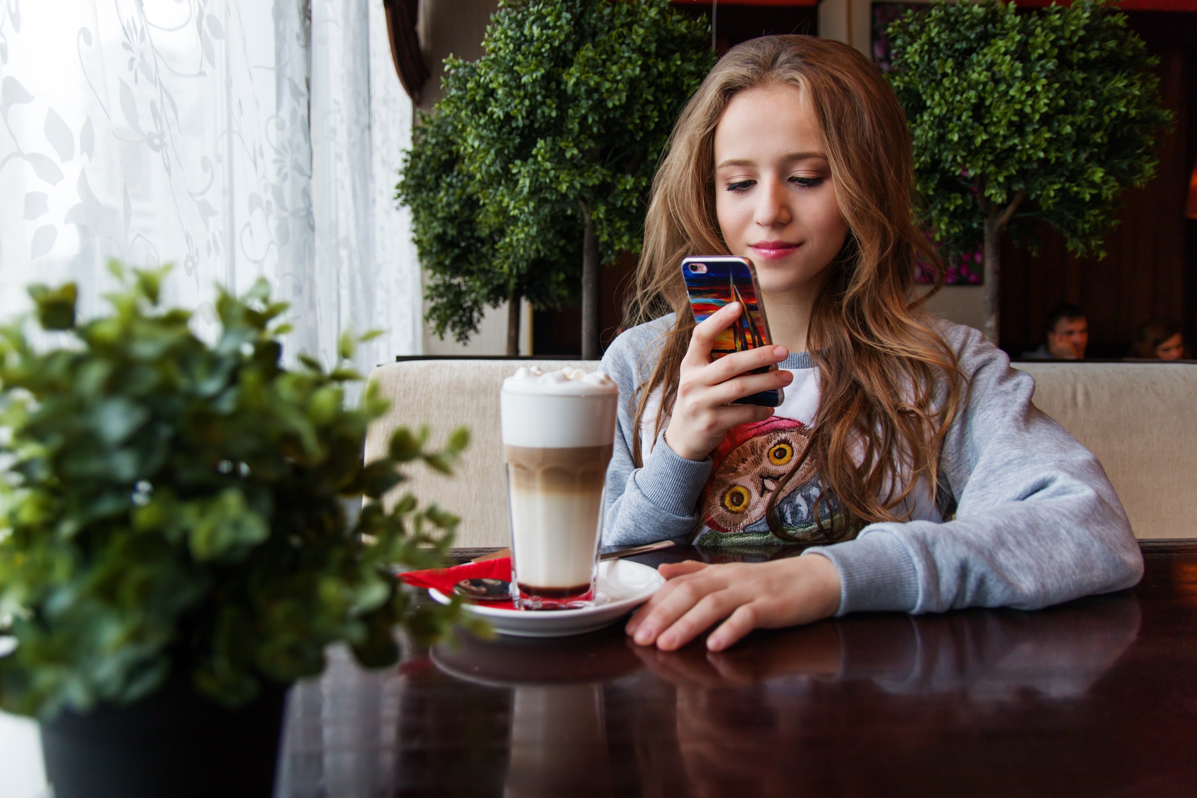 Una jovencita en una cafetería con su celular. | Foto: Pexels