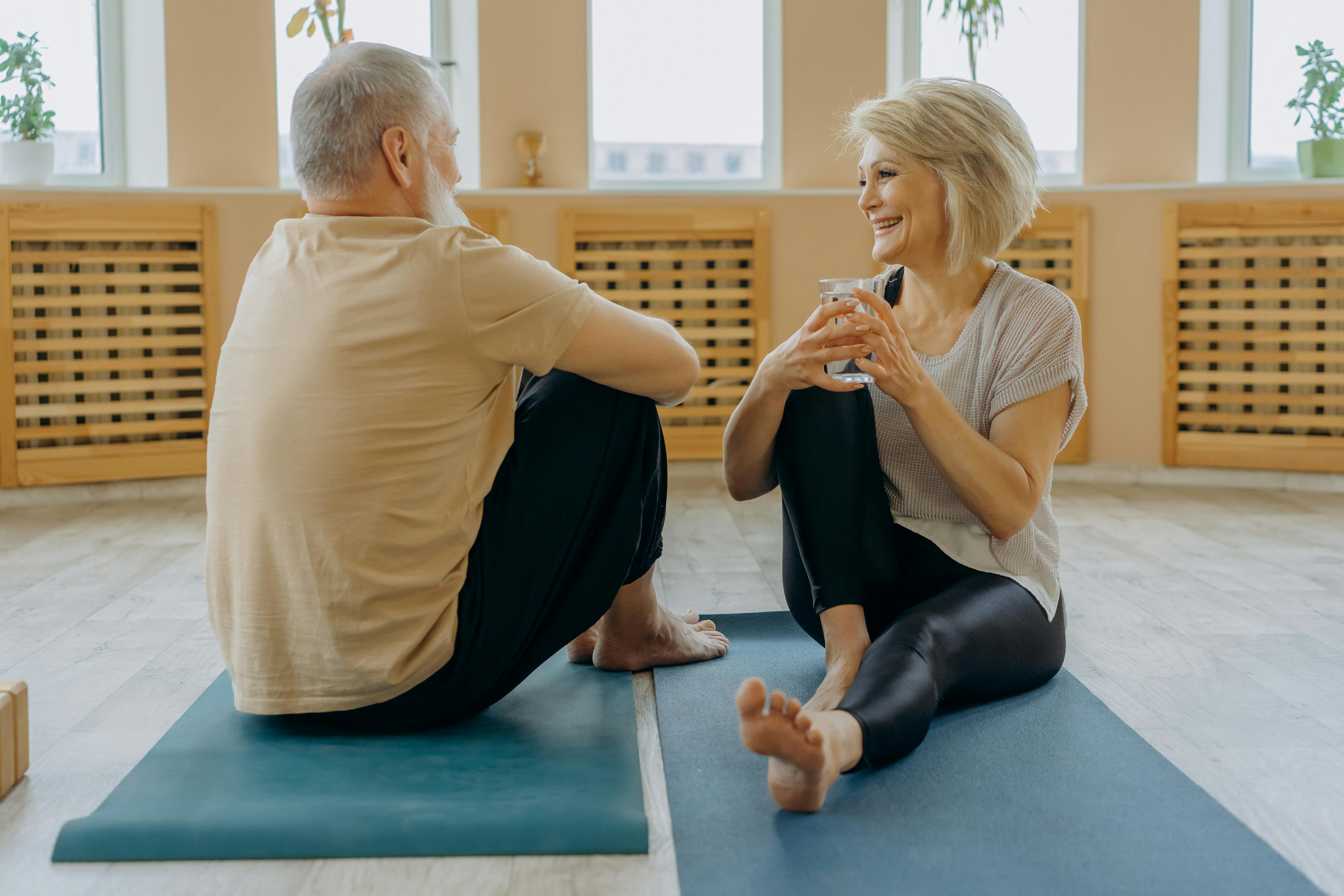 An elderly man and woman having a conversation while siting on a yoga mat | Source: Pexels