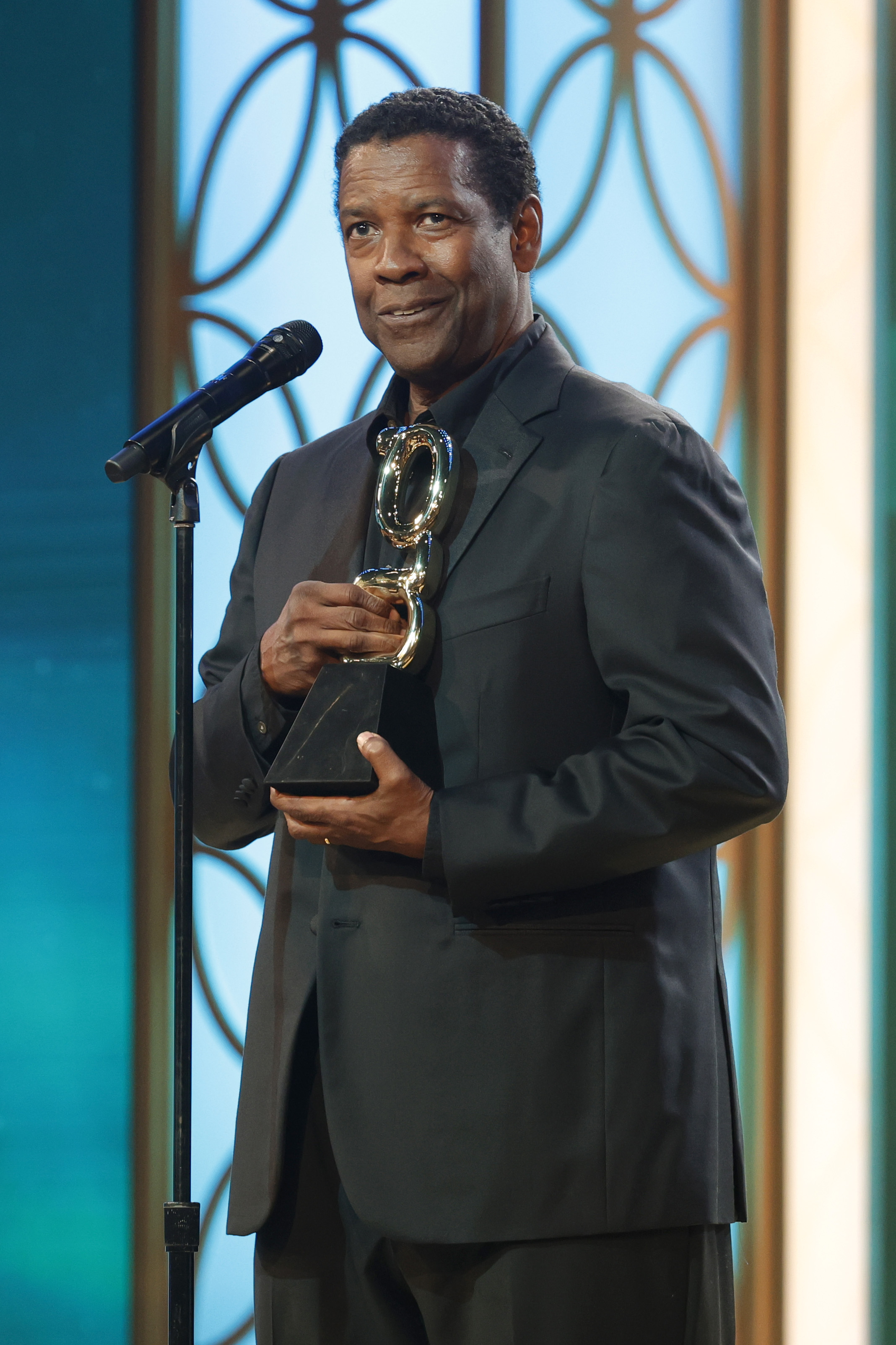 Denzel Washington accepts the Film Icon Award at the Grio Awards. His black hair is slightly trimmed and coily. Dressed in a black suit, his mature, distinguished look mirrors the honor he received that evening.