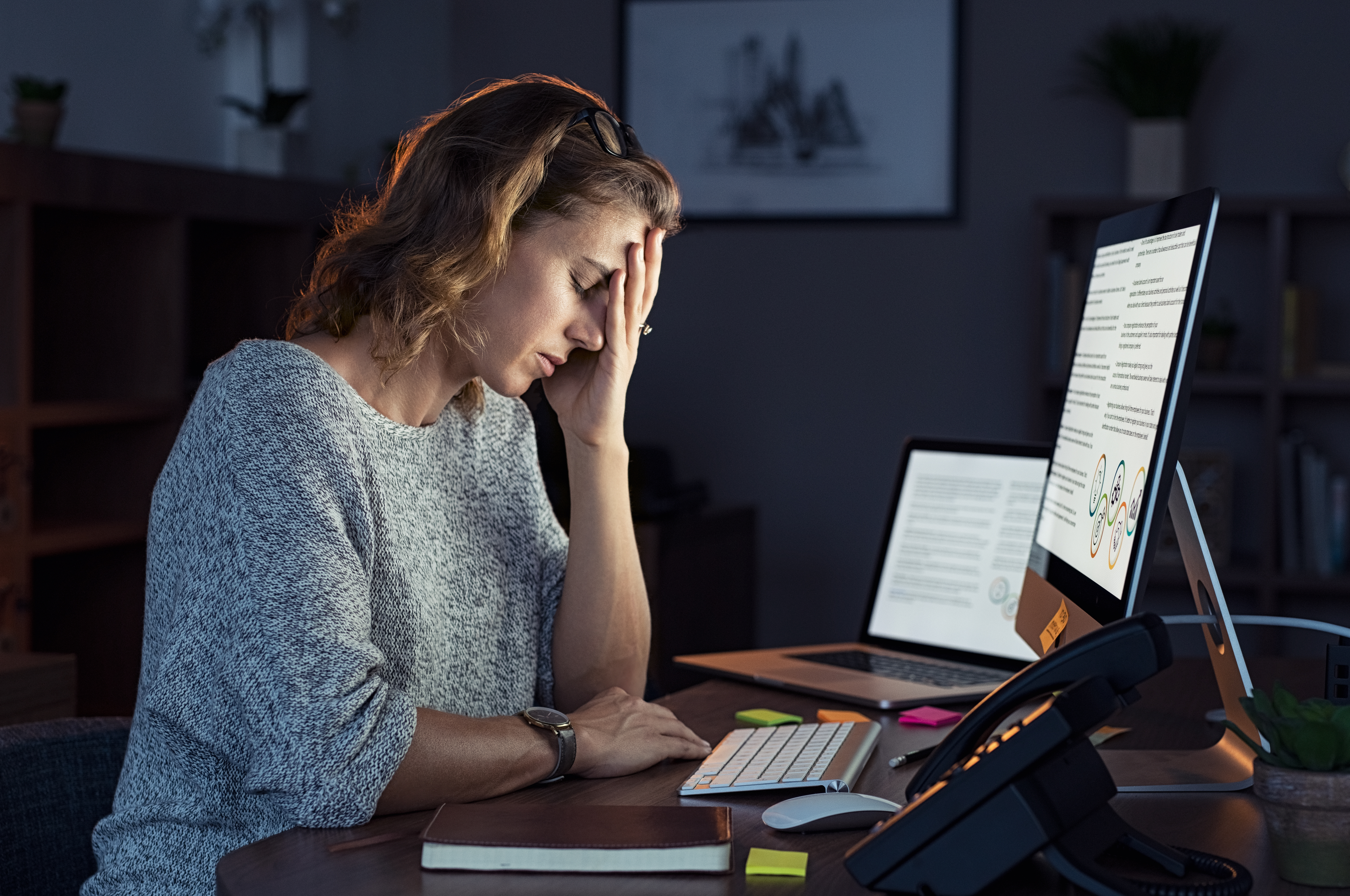 Portrait of a casual stressed lady with headache at desk. | Source: Shutterstock