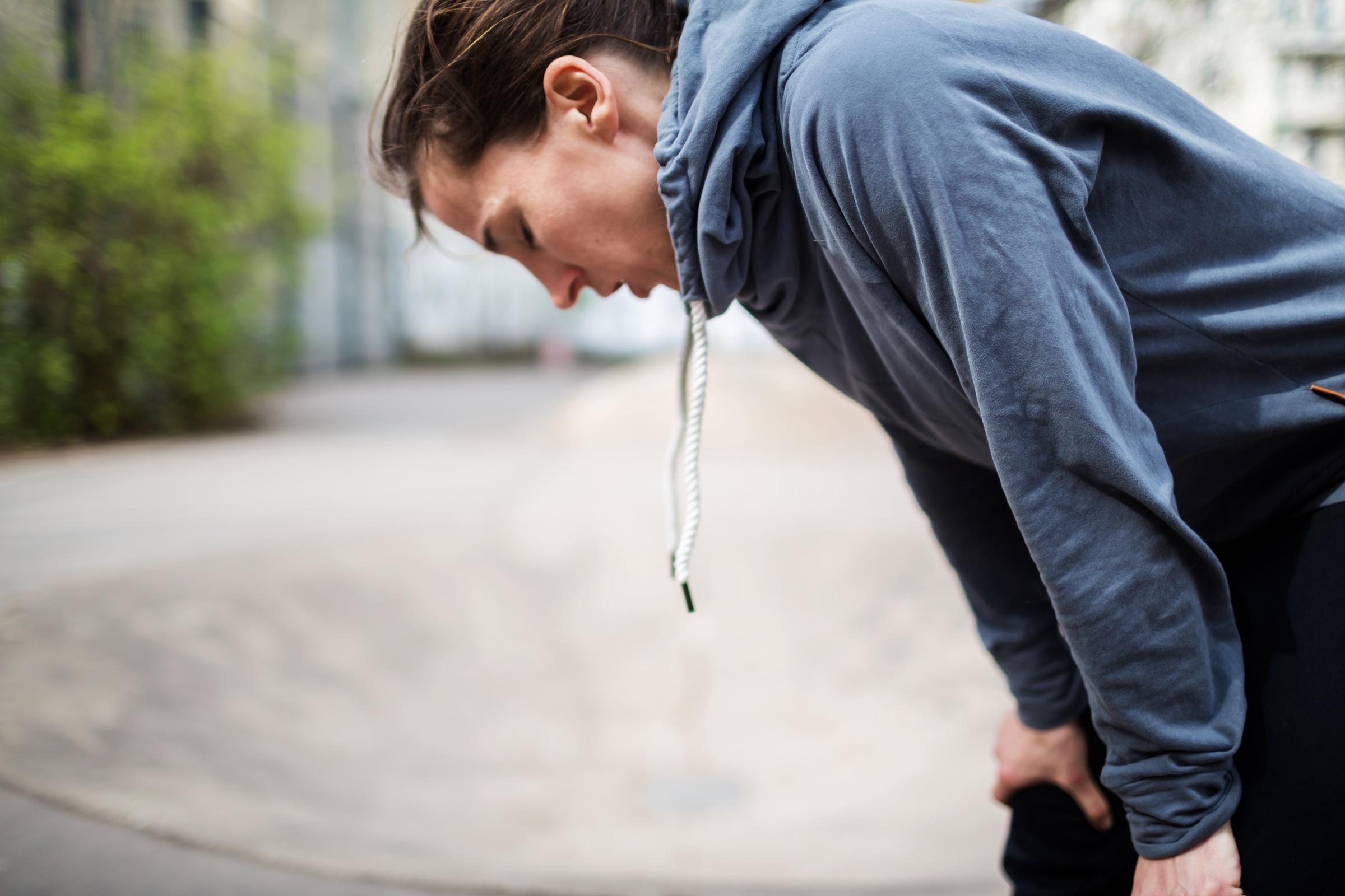 Exhausted woman leaning forward with hands on her knees, appearing fatigued | Source: Getty Images