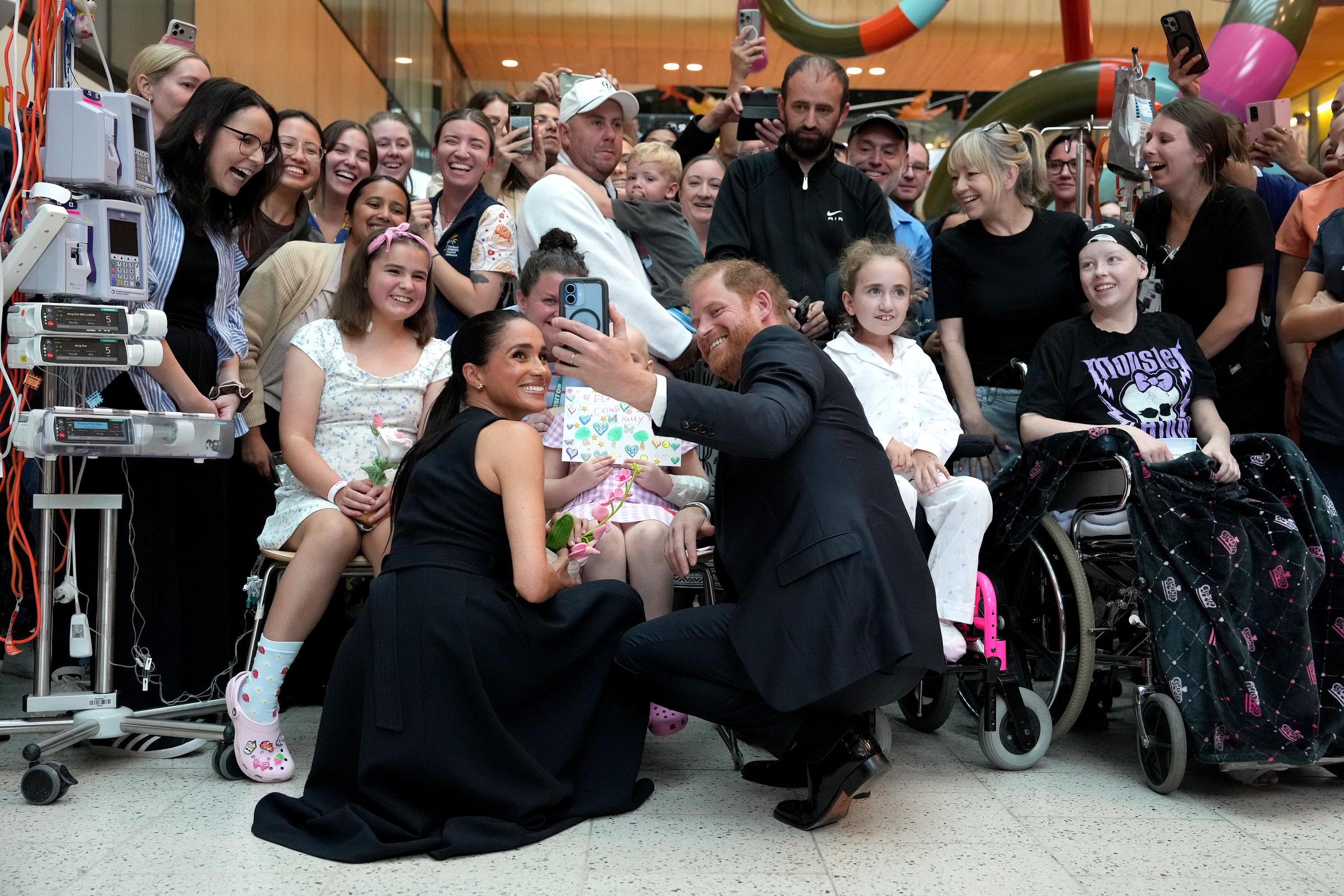 Meghan Markle and Prince Harry joined patients, families, and staff for a group photo, with the Duke holding up a phone to capture the moment during their Melbourne visit on 14 April 2026. | Source: Getty Images