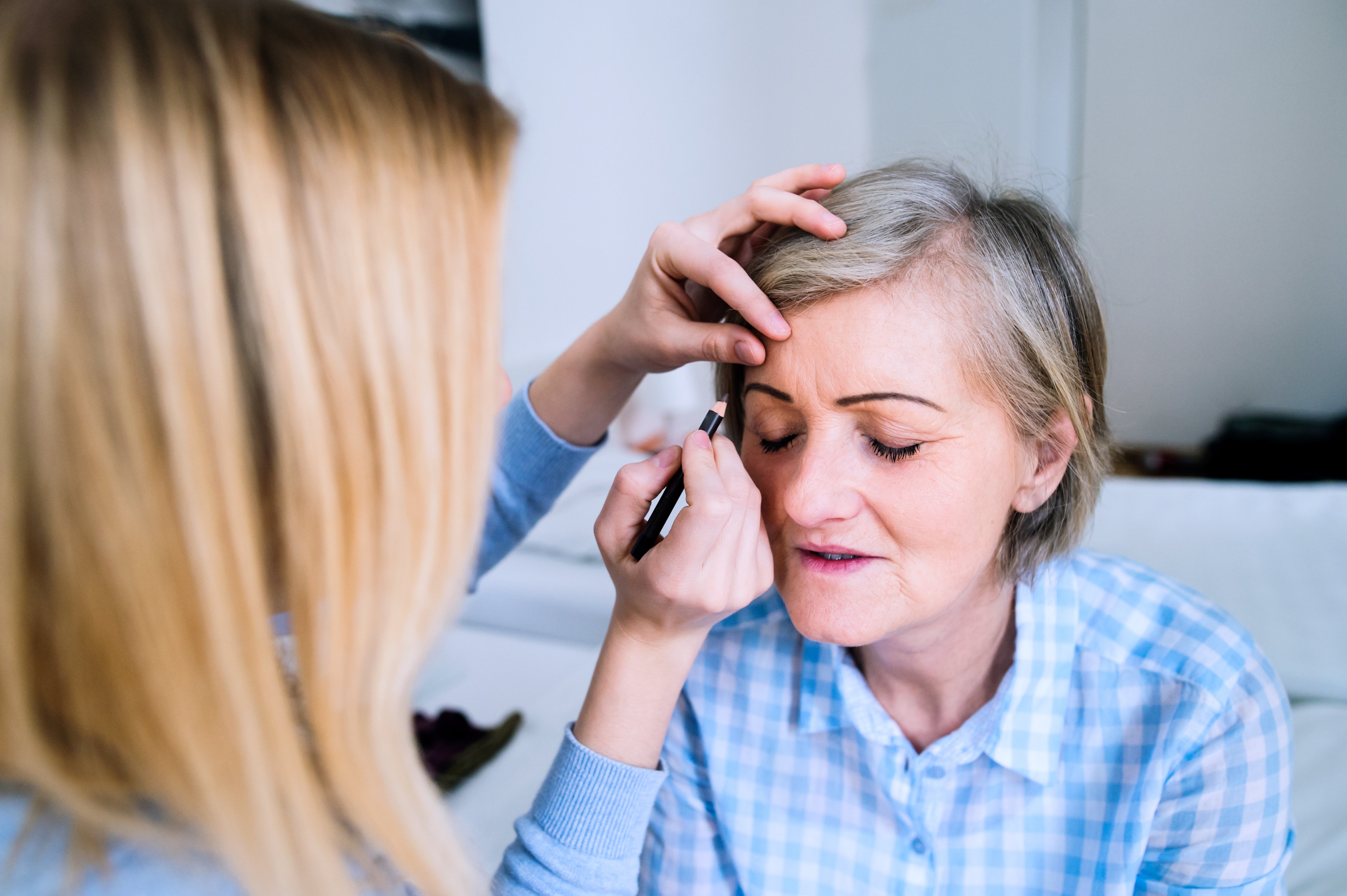 Mujer aplica maquillaje en las cejas a mujer mayor. | Foto: Shutterstock