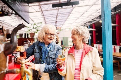 Photo of two elderly women holding wineglass and smiling while looking at each other in restaurant | Photo: Getty Images