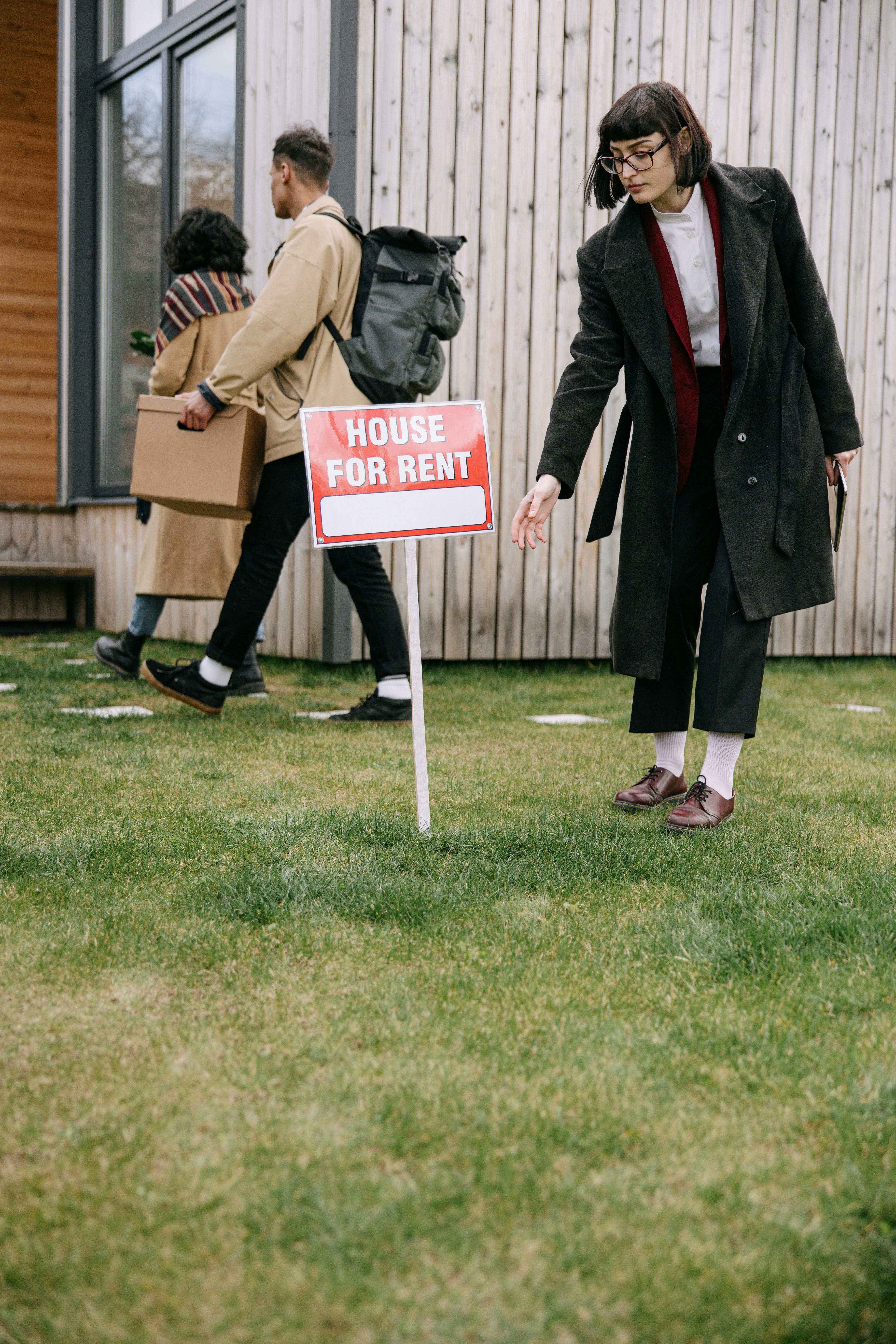 A woman in a black coat beside a "House for rent" sign | Source: Pexels