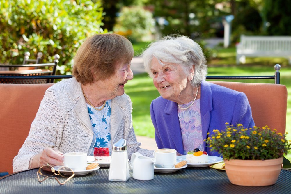 Dos mujeres mayores felices sentadas, charlando en la mesa al aire libre con café y bocadillos. Fuente: Shutterstock Dos mujeres mayores felices sentadas, charlando en la mesa al aire libre con café y bocadillos. Fuente: Shutterstock