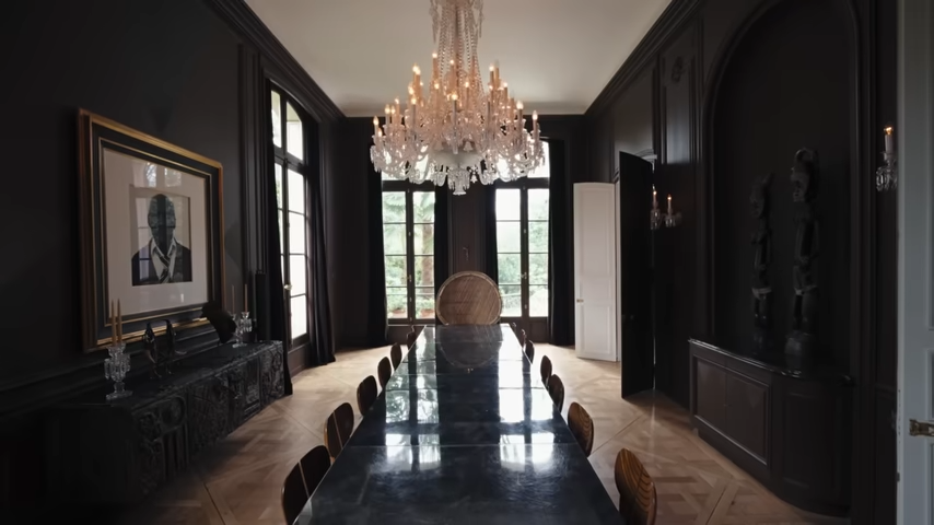 The dramatic, dimly lit dining room features a long, high-gloss Karl Springer table, Scarpa "Africa" chairs, and a commanding portrait of his grandfather, Albert Roker. | Source: YouTube/@Archdigest