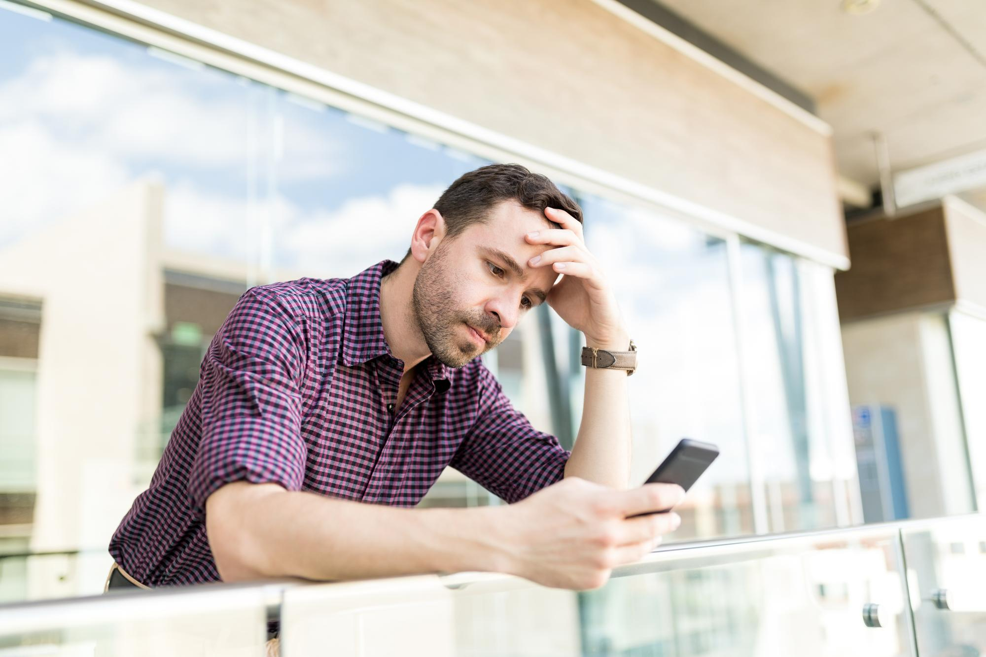 An upset man standing over a balcony looking at his phone | Source: Freepik
