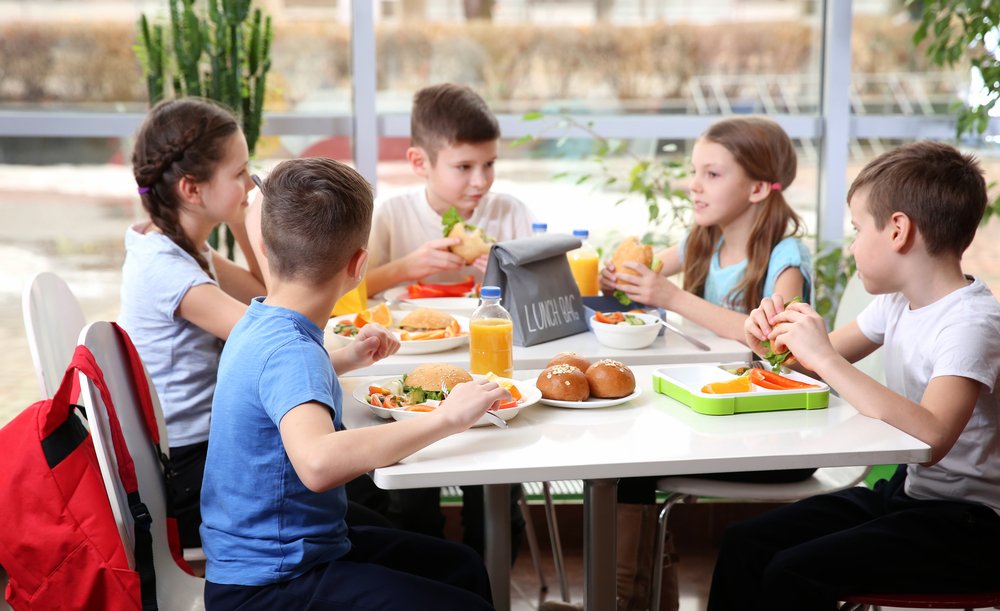 Niños sentados en la mesa de la cafetería mientras almuerzan. | Fuente: Shutterstock. Niños sentados en la mesa de la cafetería mientras almuerzan. | Fuente: Shutterstock.