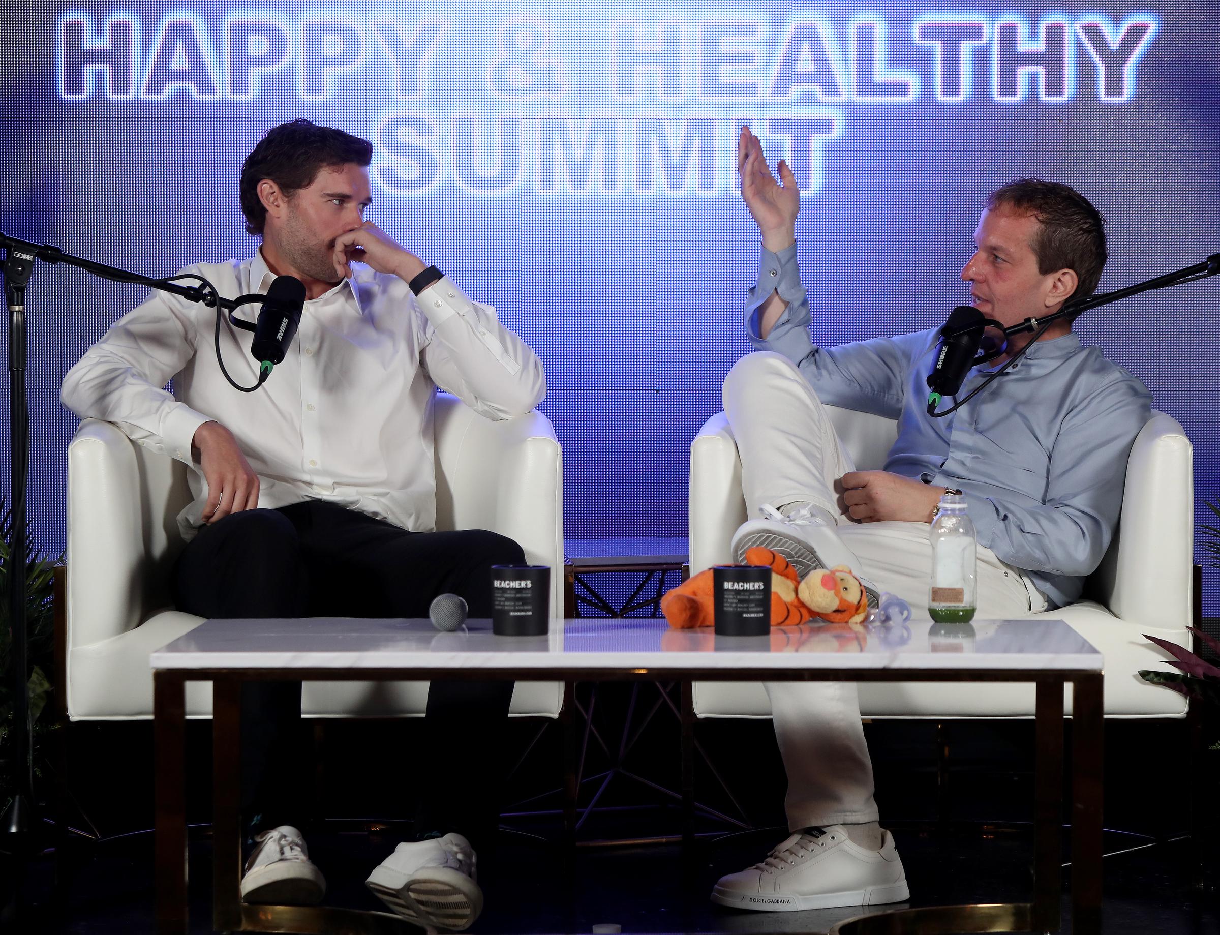 Christopher Schwarzenegger listens thoughtfully as Jeff Beacher makes a point during their panel segment. The two sit across from each other on stage, deep in discussion about personal growth and health.