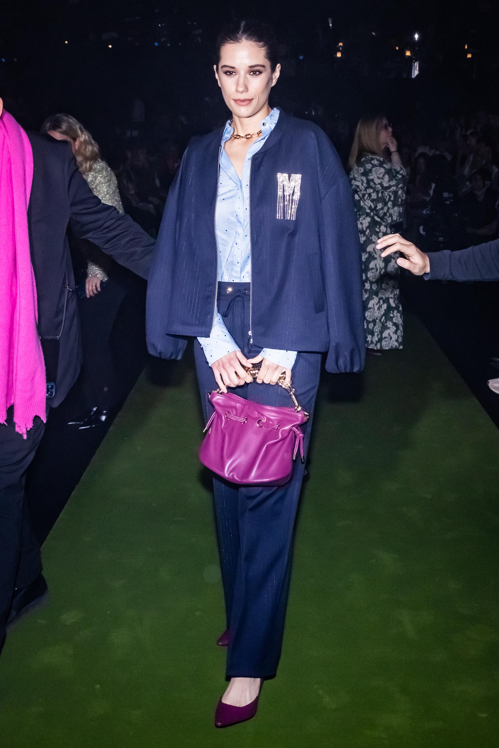 Ella Bleu Travolta walks the fashion circuit in Madrid in 2025, wearing a navy layered outfit with a bright magenta handbag. Her appearance at Mercedes-Benz Fashion Week highlighted her increasingly editorial style.