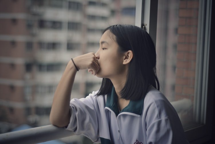 A lady in deep thoughts and seating by a window | Photo: Unsplash