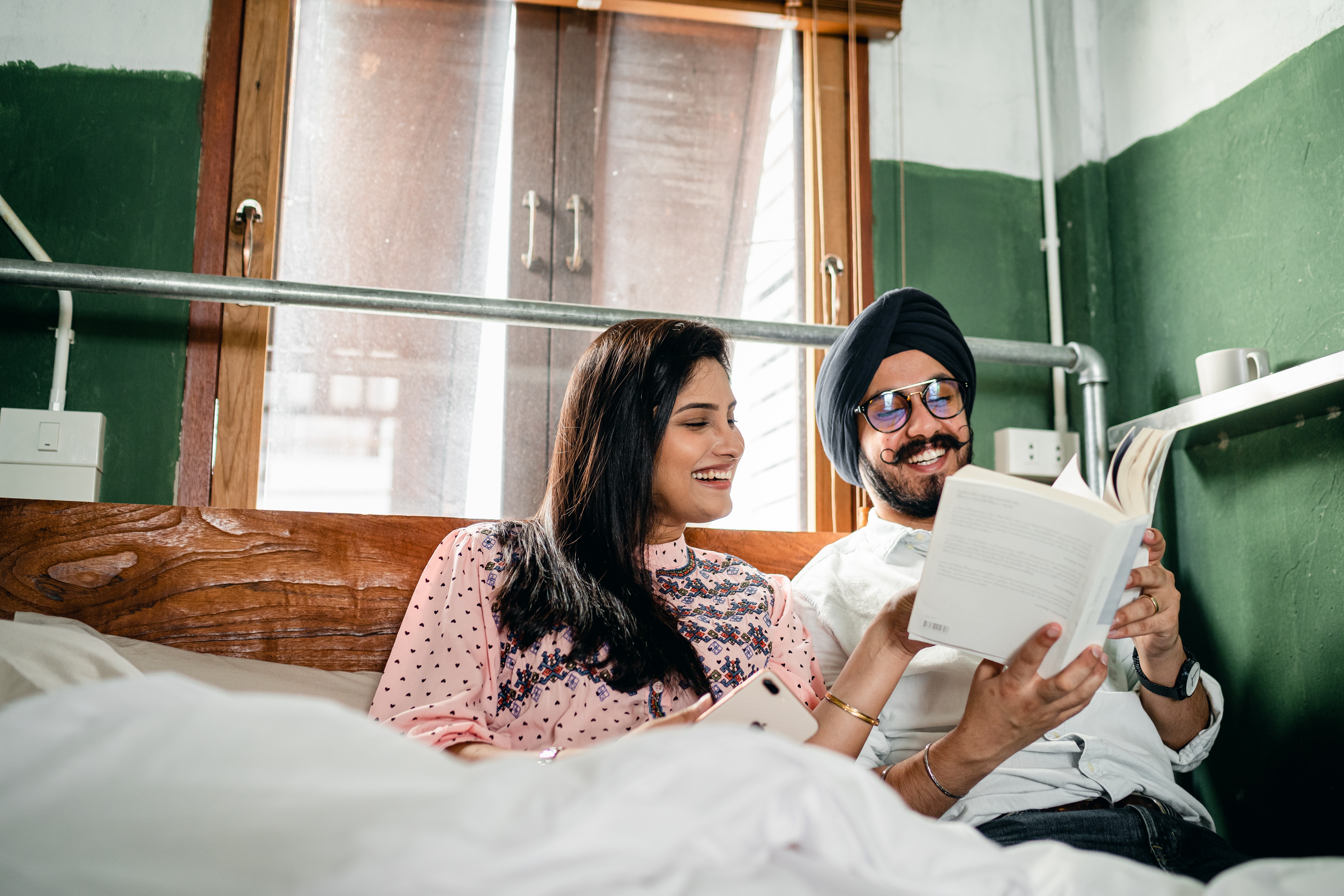 A couple reading and laughing in bed together. | Source: Pexels