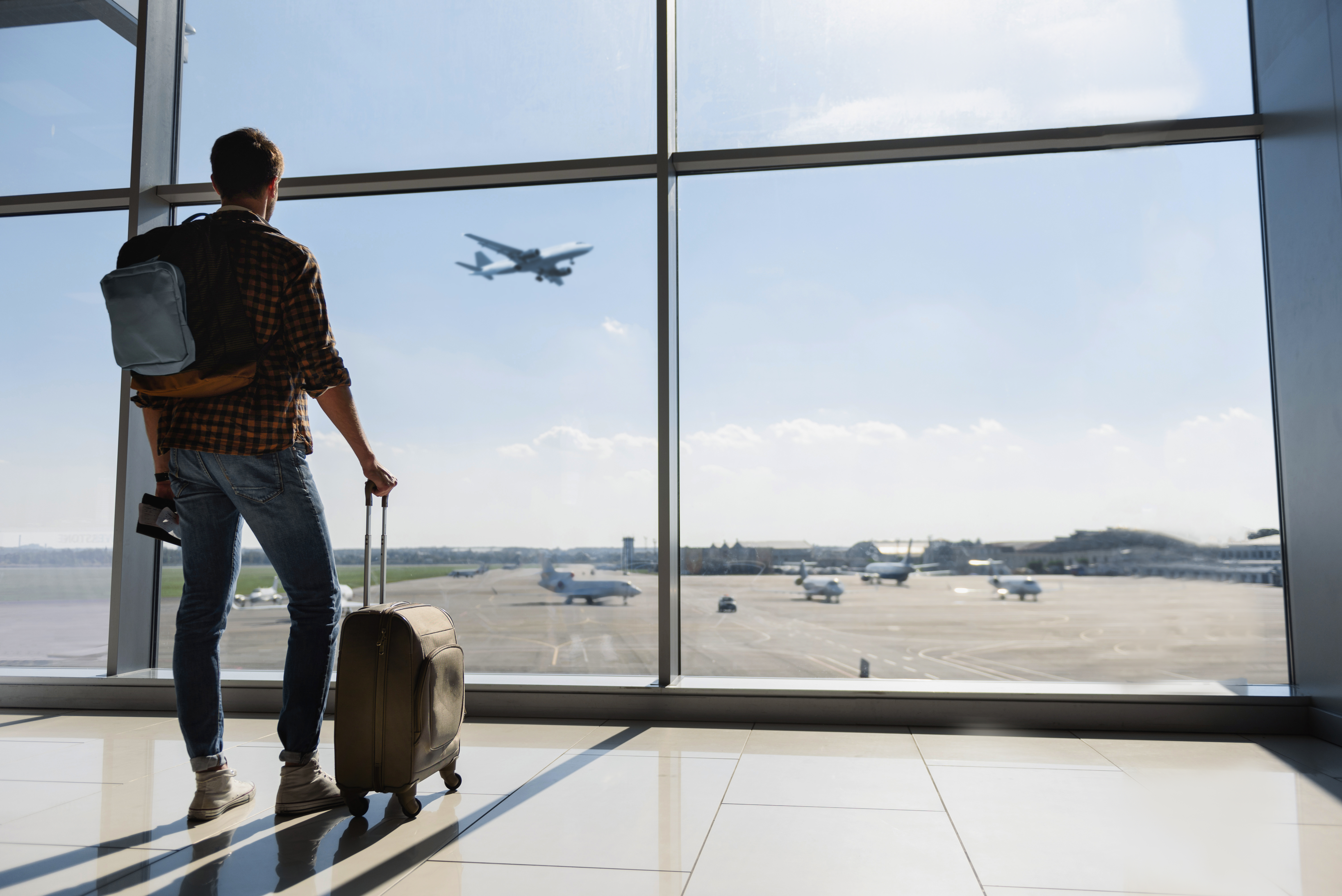 A young man with luggage stands near the window at the airport and watches an airplane before departure | Source: Shutterstock