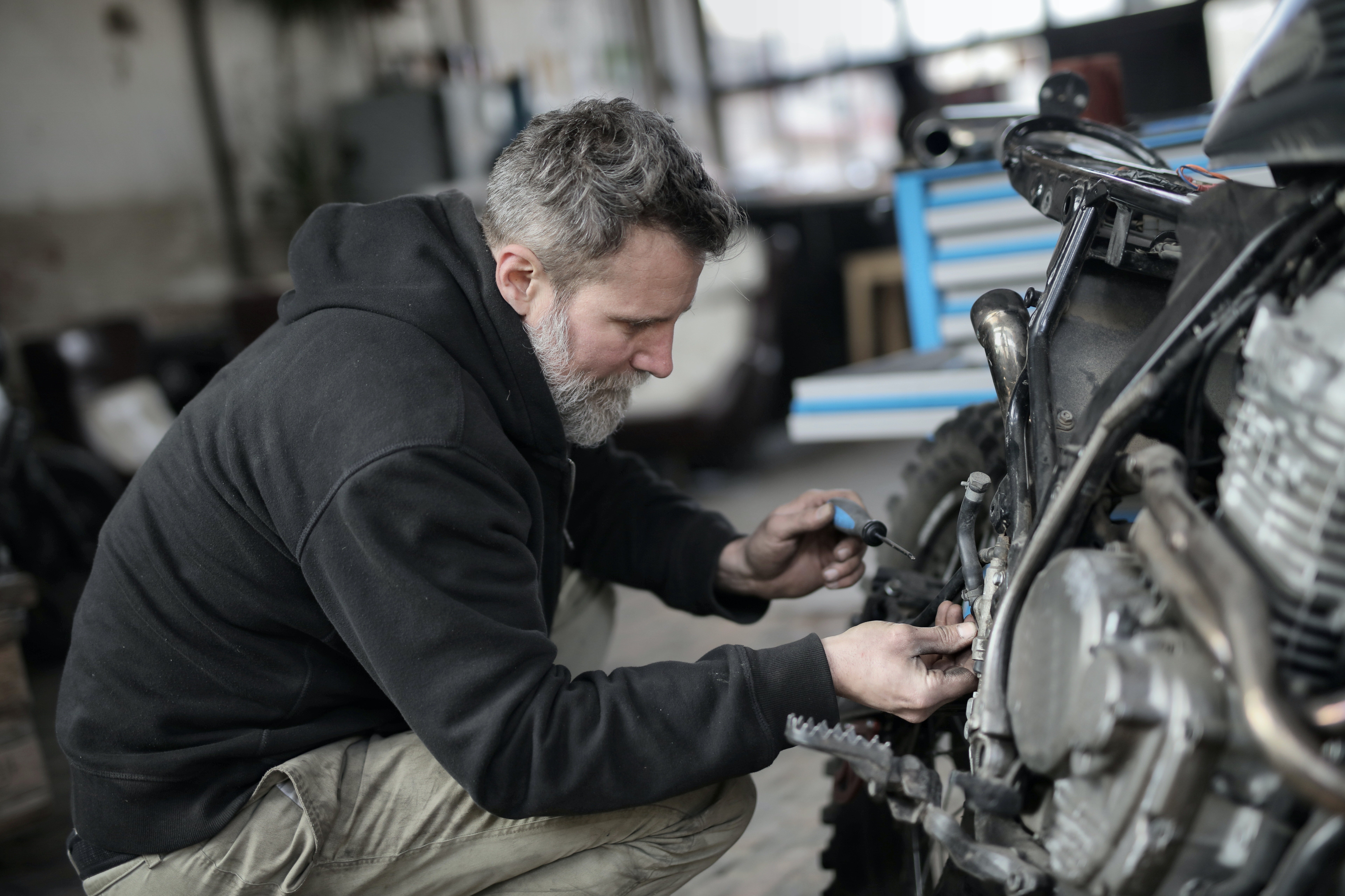 A bearded man fixing a motorcycle in a workshop. | Photo: Pexels/Andrea Piacquadio