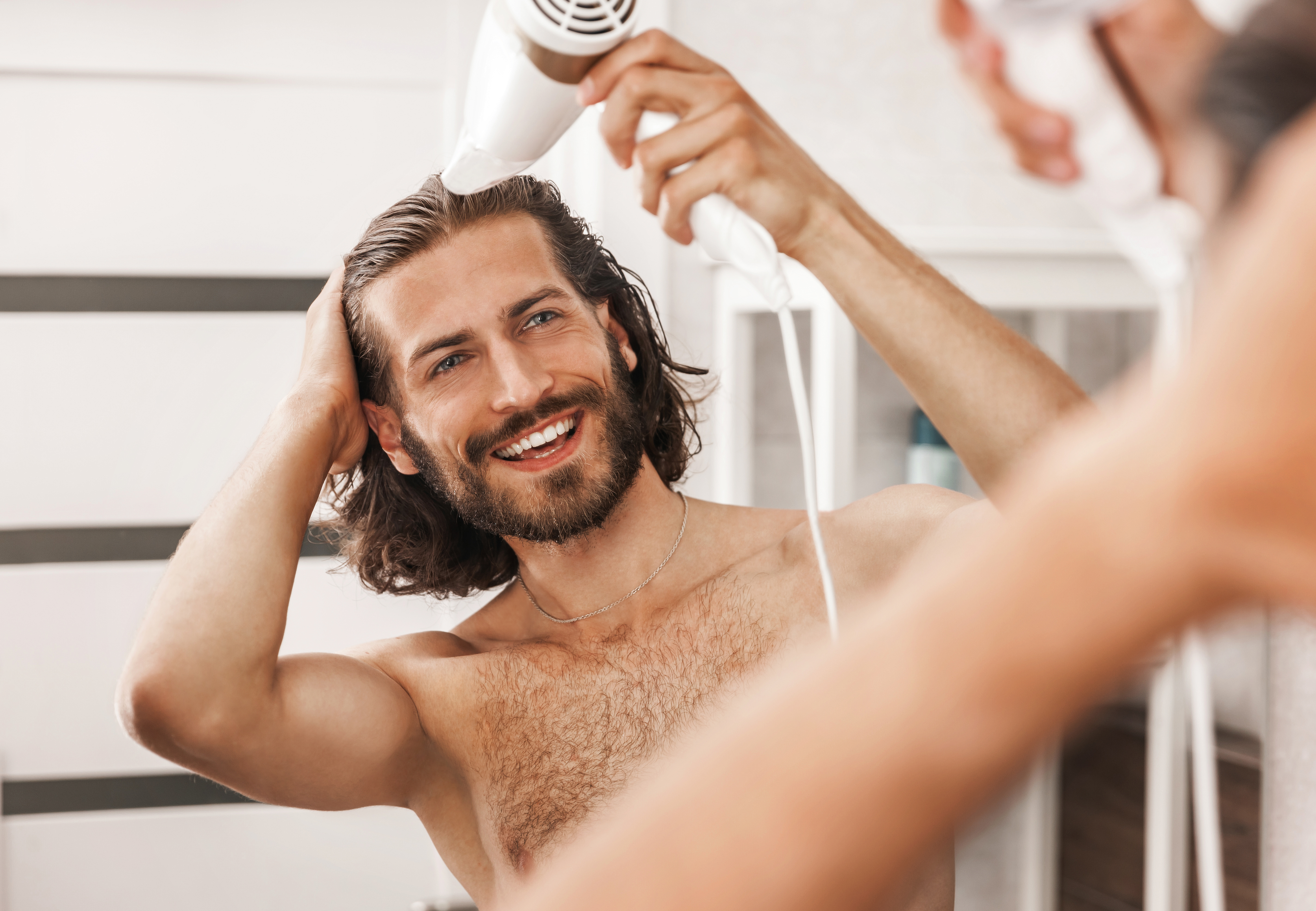 A man using a hair dryer in front of a mirror |Source: Shutterstock