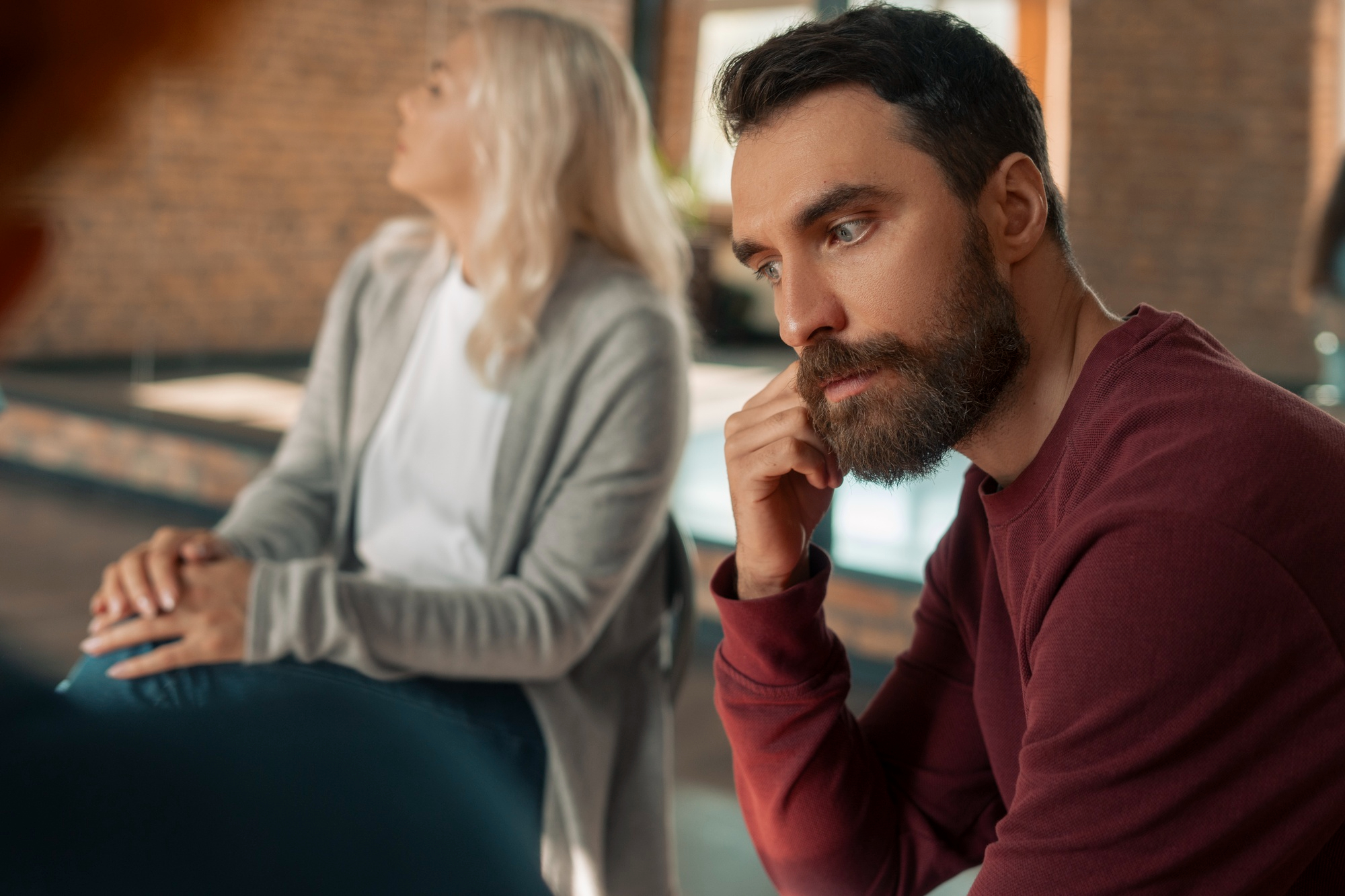 A woman looking upset while a guilty man looks away while someone else appears blurred out | Source: Freepik