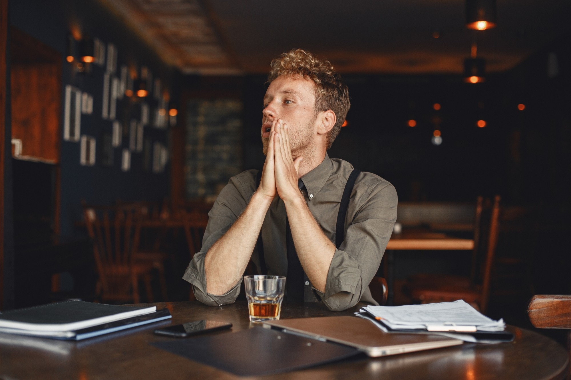 A shocked man covering part of his face while sitting with a drink and papers in front of him | Source: Freepik