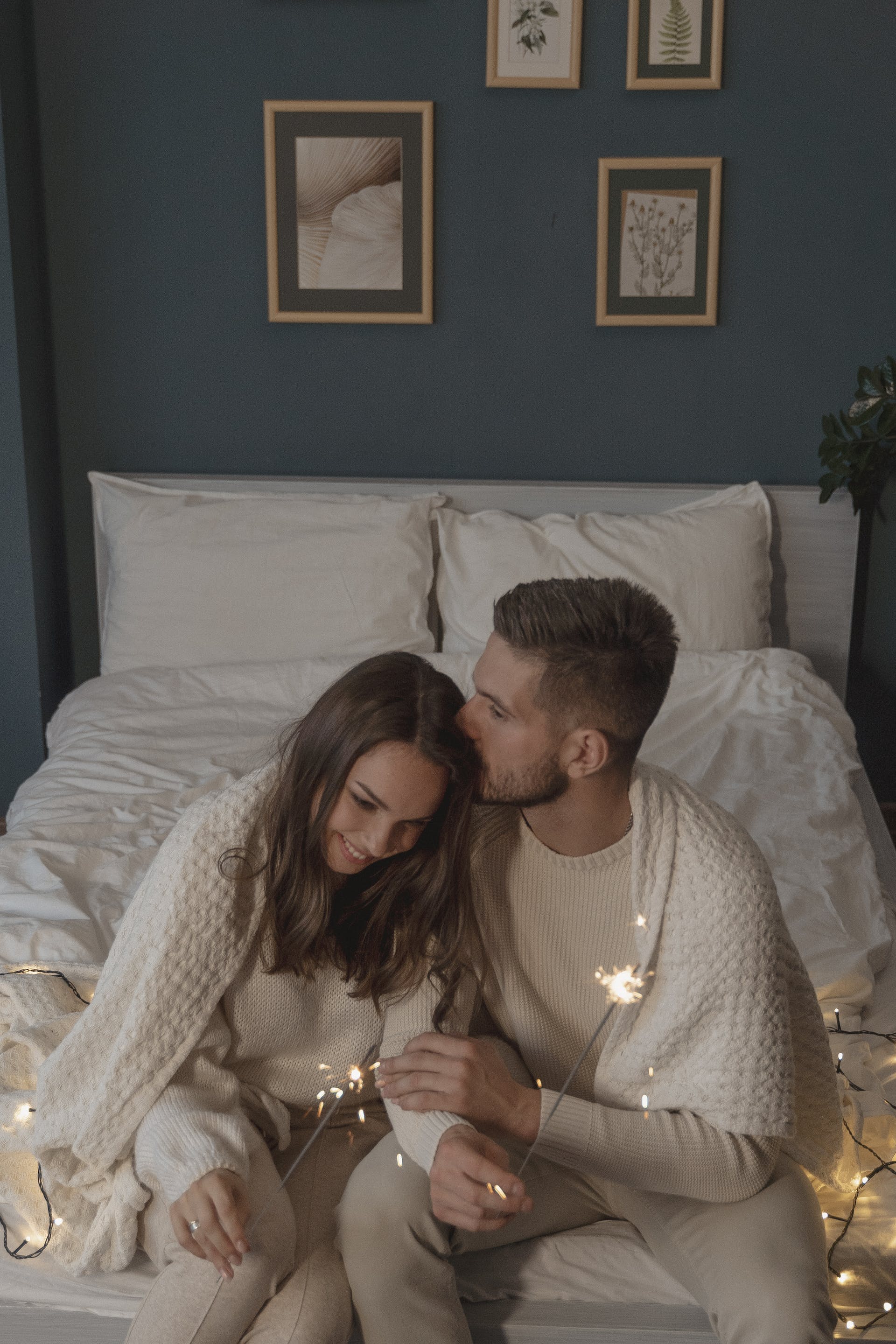 A man kissing a woman on top of her head in their bedroom while holding sparklers | Source: Pexels