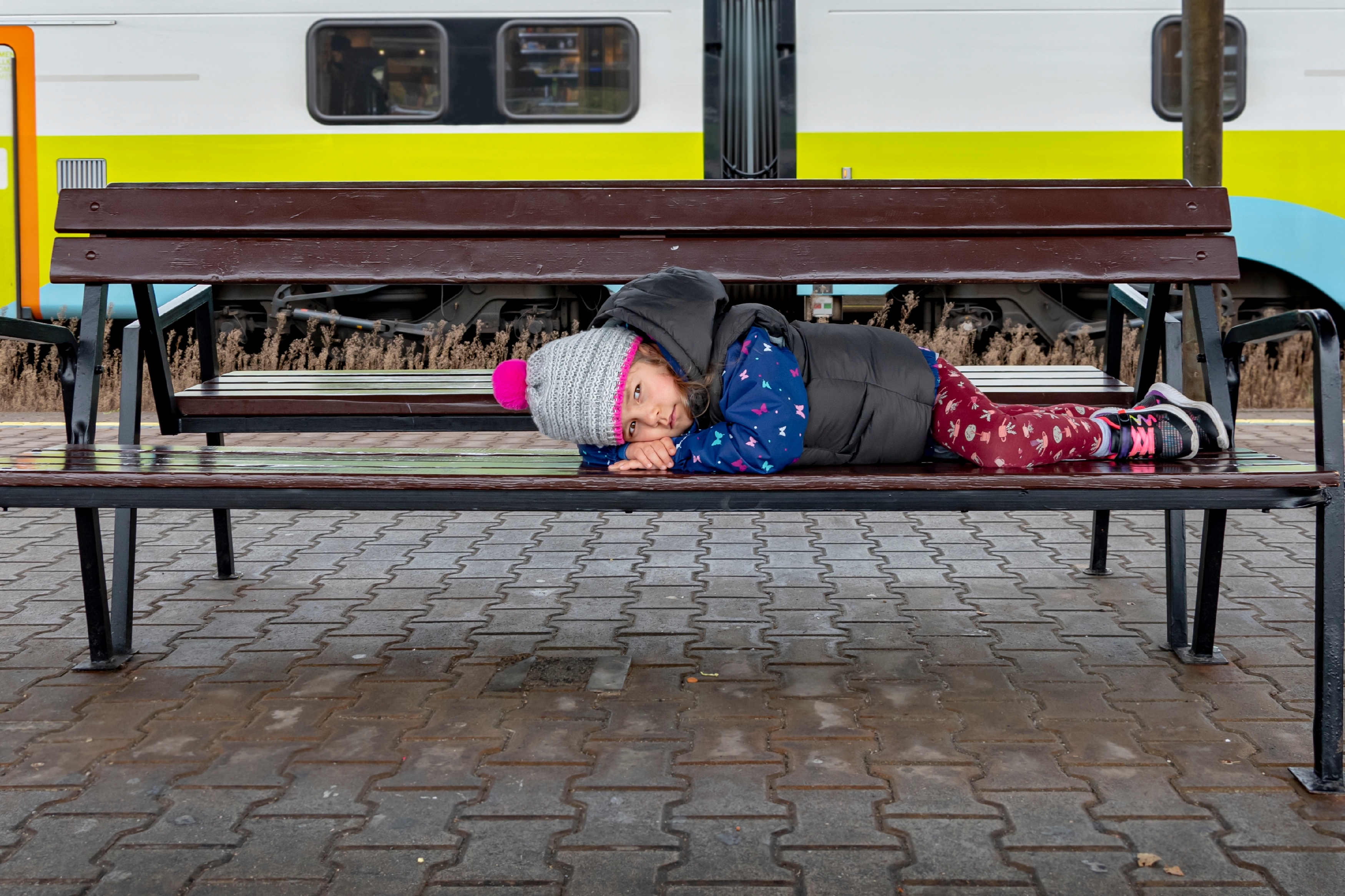 Lonely little girl lying on a wooden bench | Source: Shutterstock