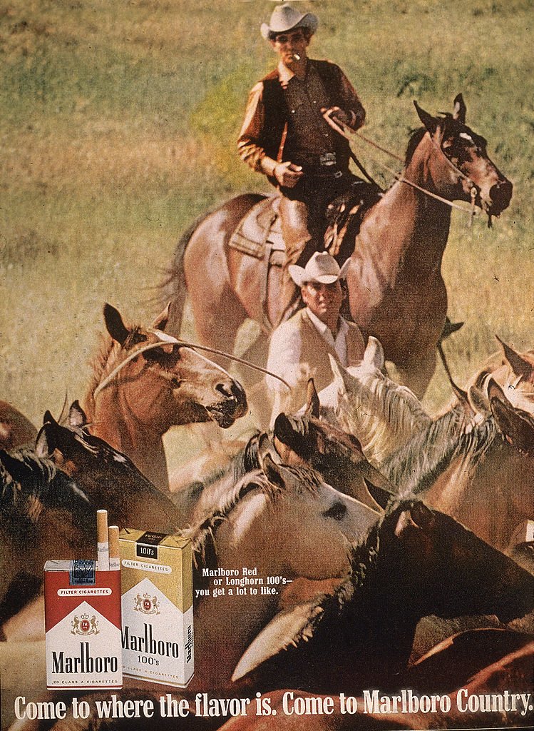 Image de deux cow-boys'Marlboro Man' rassemblant des chevaux dans une publicité pour des cigarettes Marlboro dans un magazine, années 1970| Source : Getty Images. Image de deux cow-boys'Marlboro Man' rassemblant des chevaux dans une publicité pour des cigarettes Marlboro dans un magazine, années 1970| Source : Getty Images.