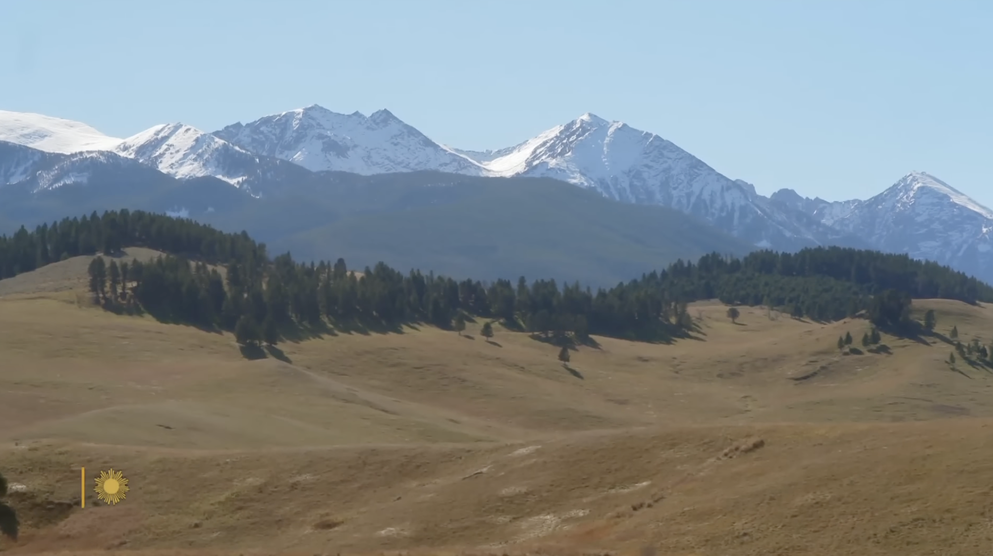 Snow-covered mountain peaks tower over rolling prairie and pine forests, highlighting the breathtaking scale of the American wilderness preserved through Ted Turner’s conservation efforts. | Source: YouTube/CBS Sunday Morning