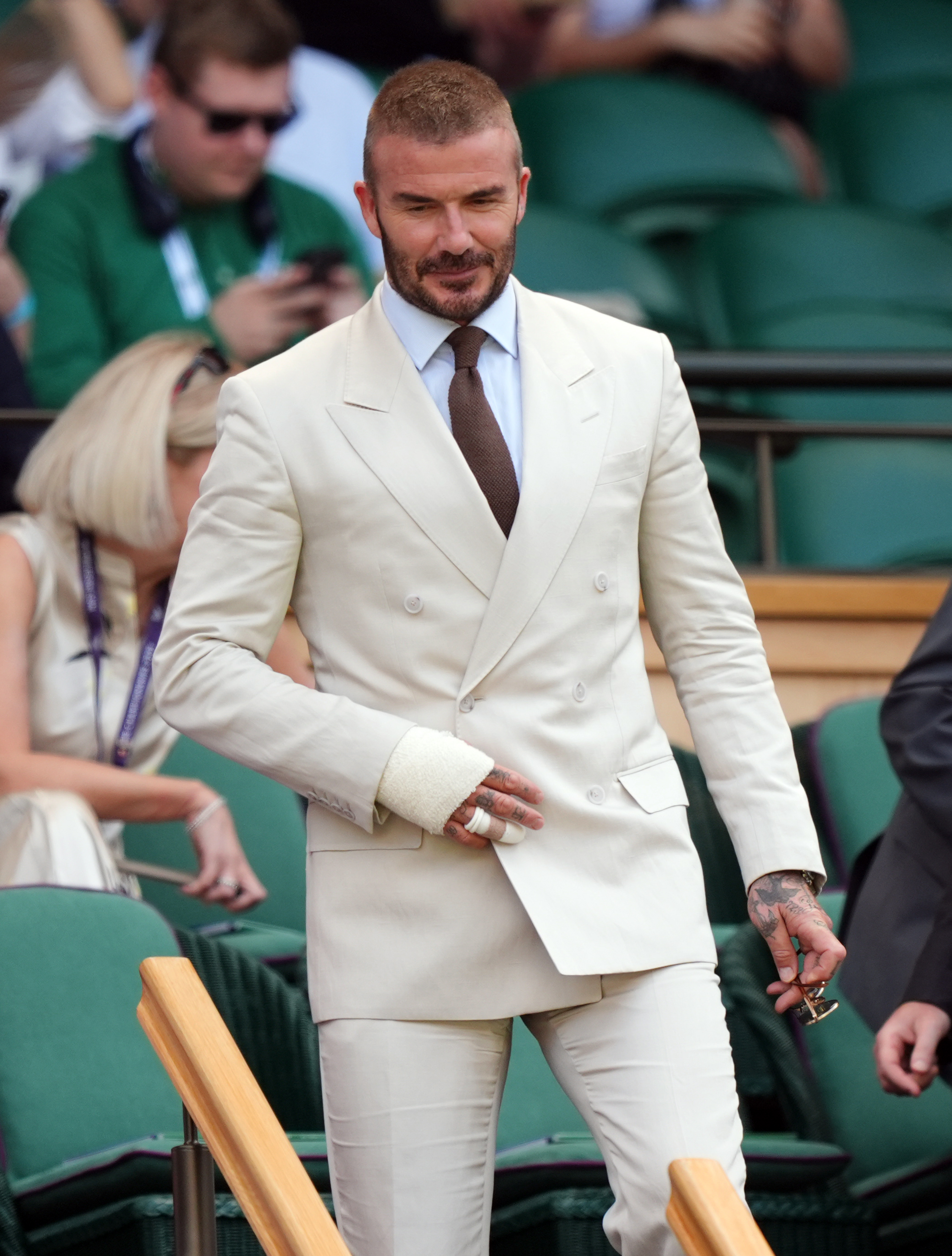 Descending into the Royal Box at Centre Court, David Beckham keeps his composure amid the buzz. With sunglasses in hand and a calm expression, the former footballer makes a stylish entrance despite his injury.