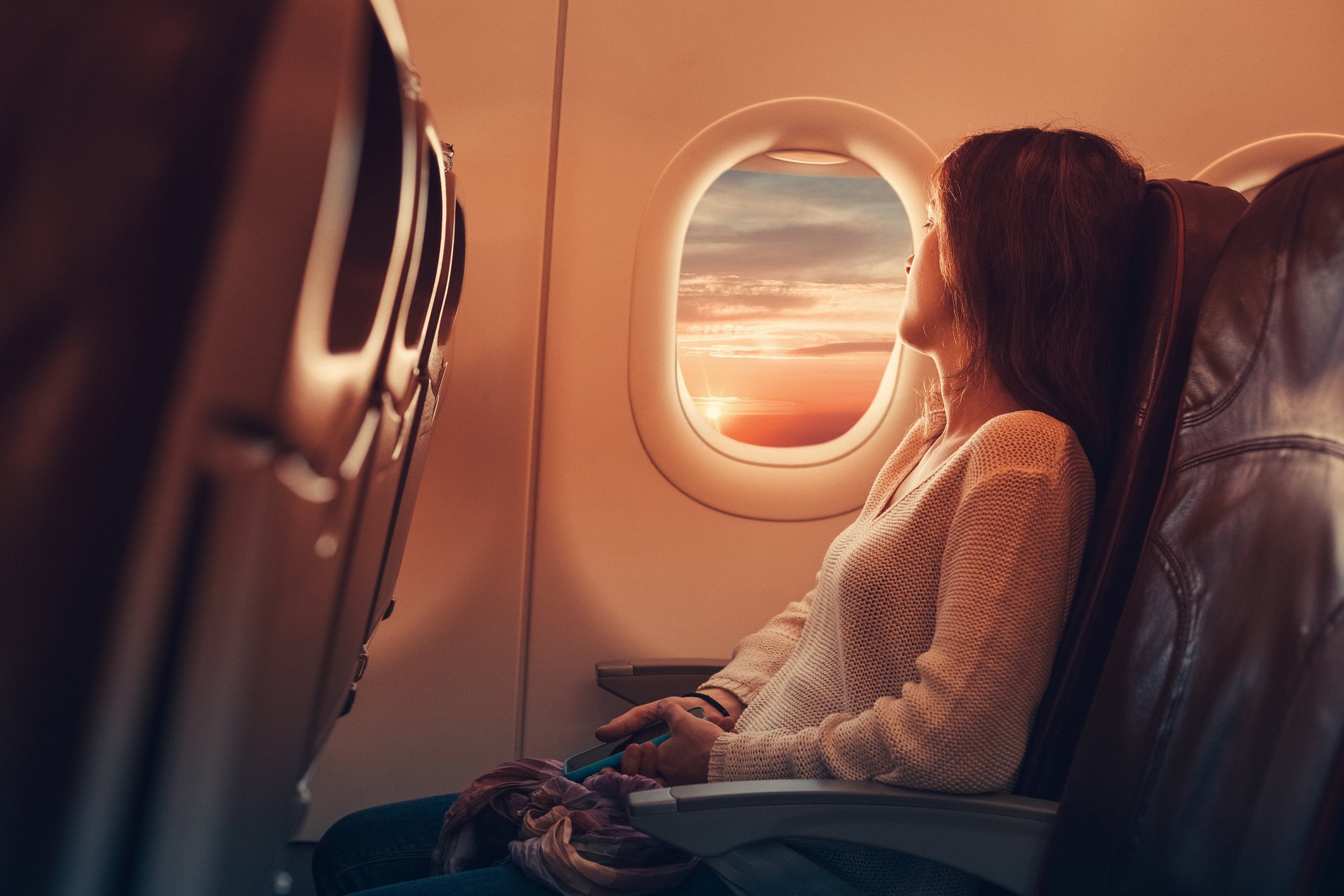 Young woman in an airplane looks through the window | Photo: Getty Images