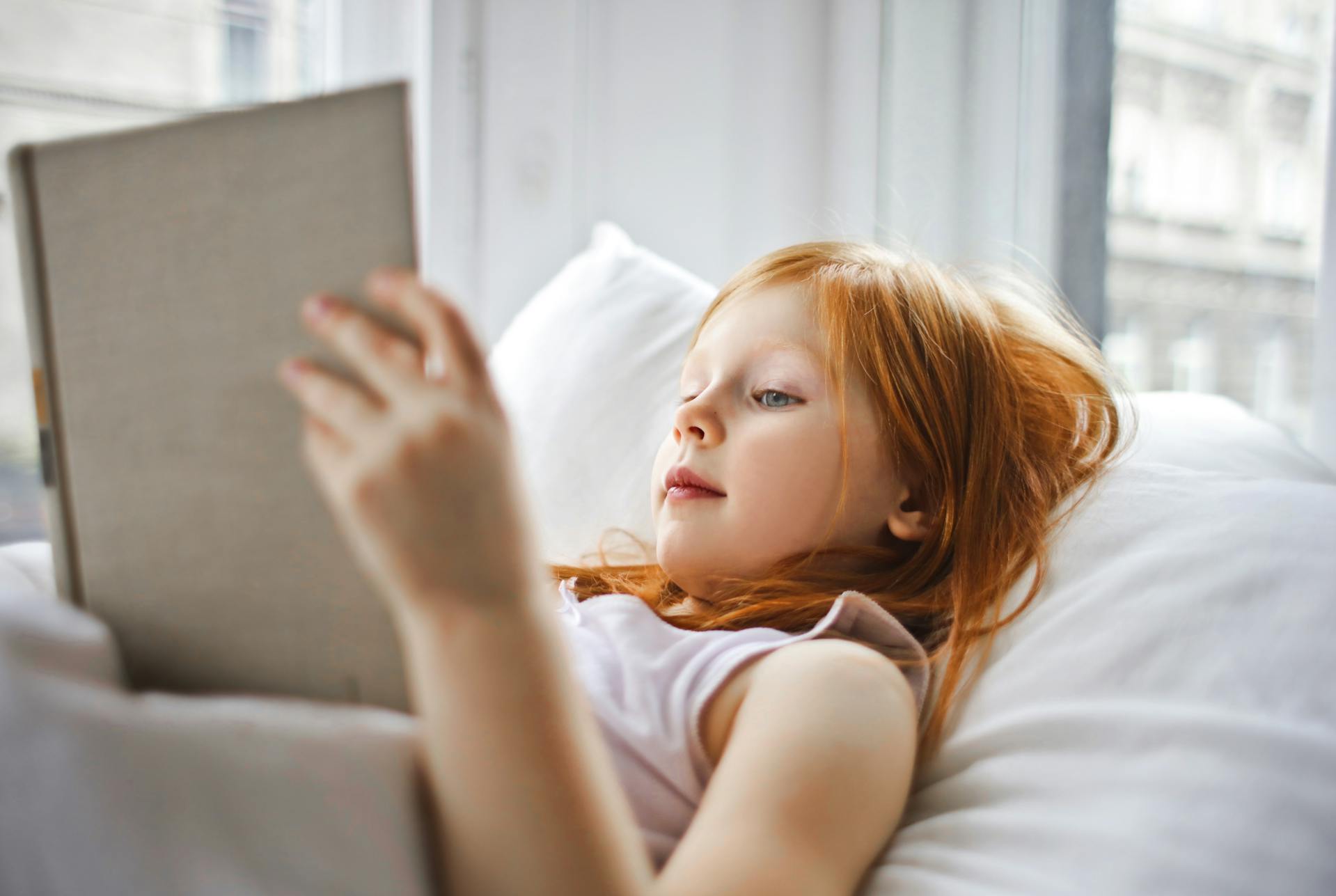 A little girl holding a book in bed | Source: Pexels