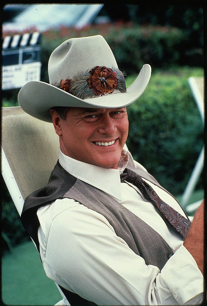 Ein Standbild aus der amerikanischen Fernsehserie 'Dallas' zeigt den Schauspieler Larry Hagman, der John Ross 'J.R.' spielt. Ewing Jr., wie er in einer Weste und Stetson auf einem Liegestuhl sitzt, Juni 1982. | Quelle: Getty Images