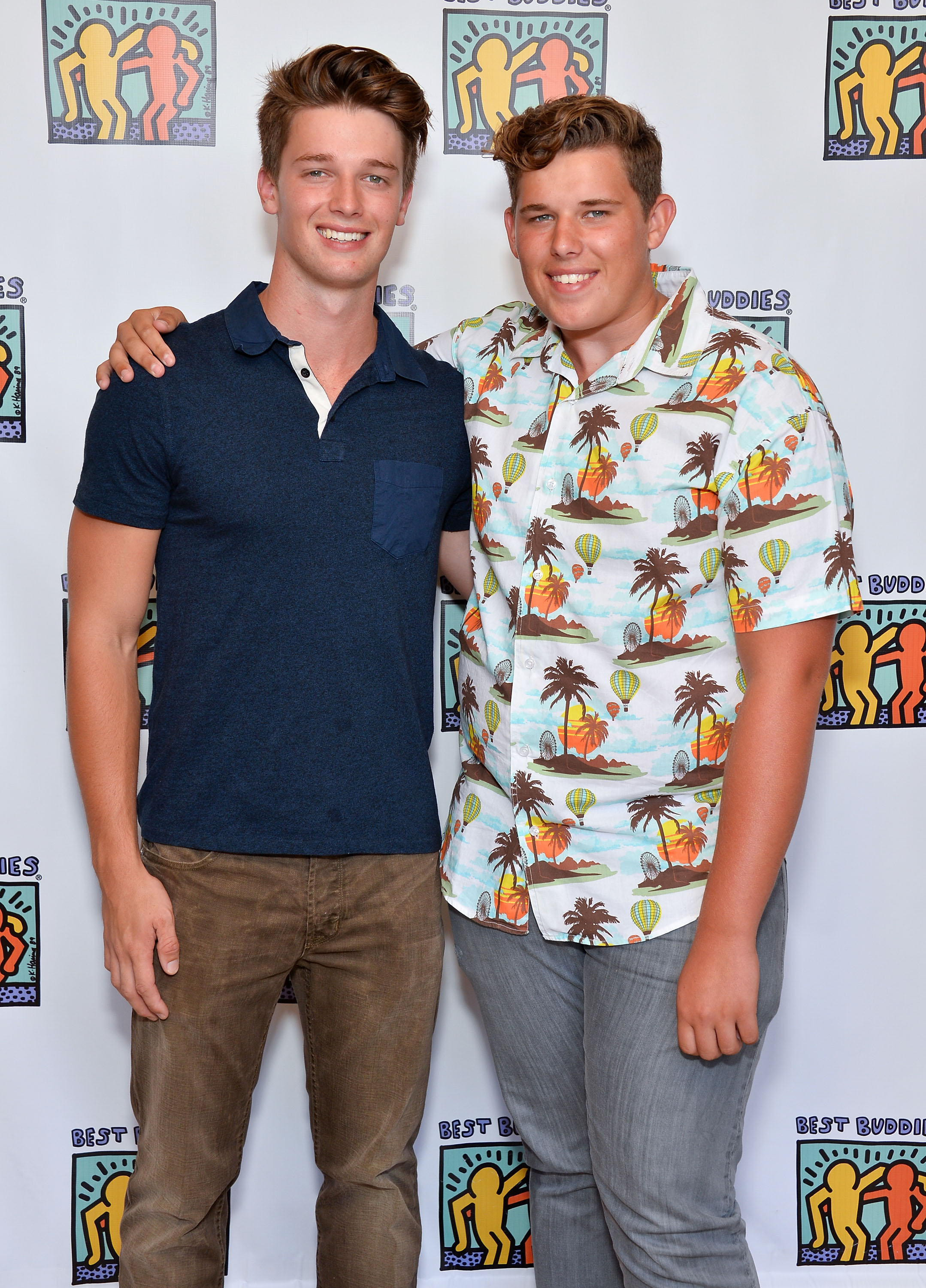 Patrick poses with his younger brother Christopher at the Team Maria benefit for Best Buddies in Beverly Hills. Patrick keeps it simple in a navy collared shirt and brown jeans, while Christopher stands out in a colorful tropical-print button-down and grey pants, smiling confidently for the camera.