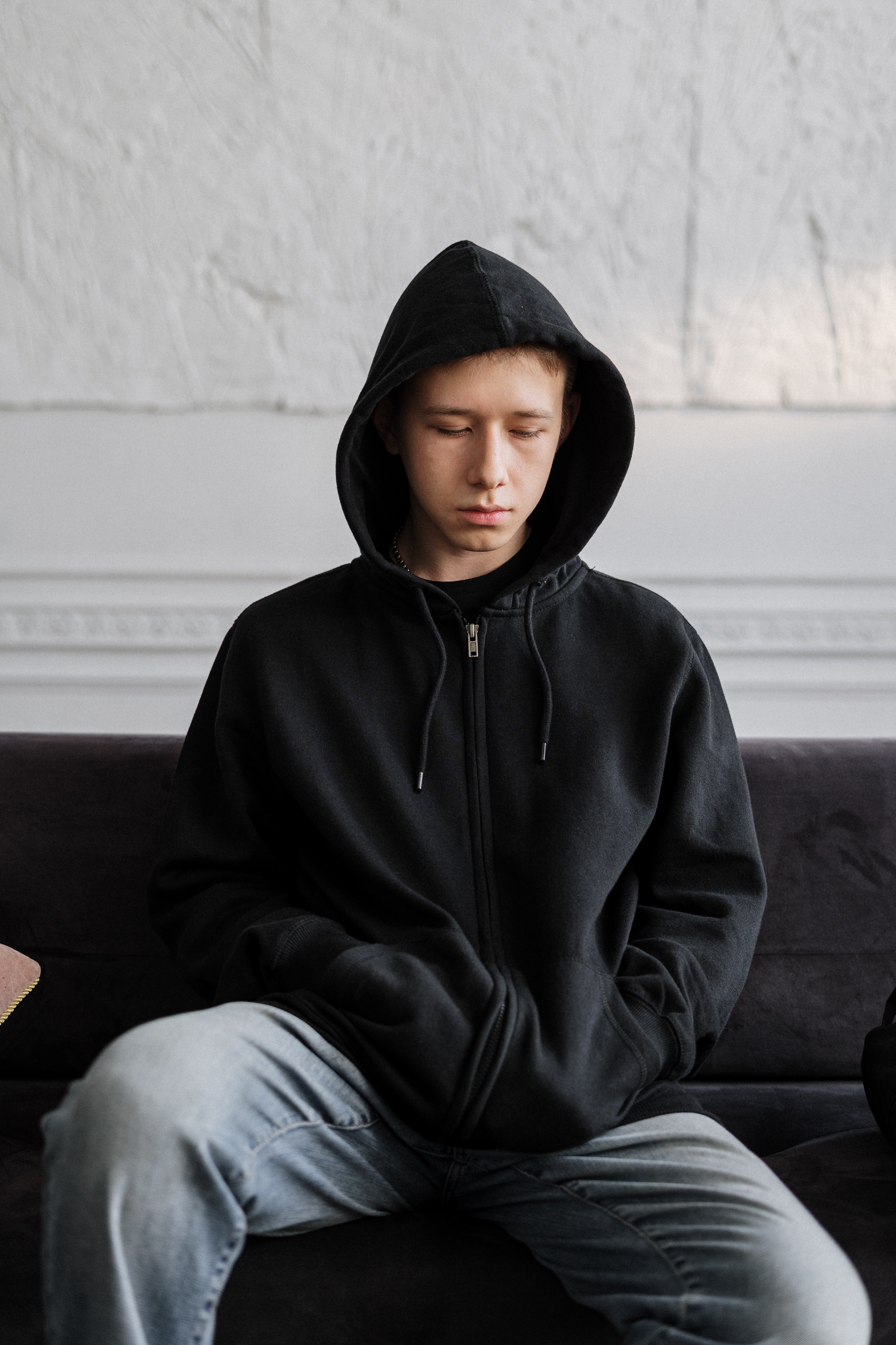 A boy in a Black hoodie sitting on a couch. | Source: Pexels